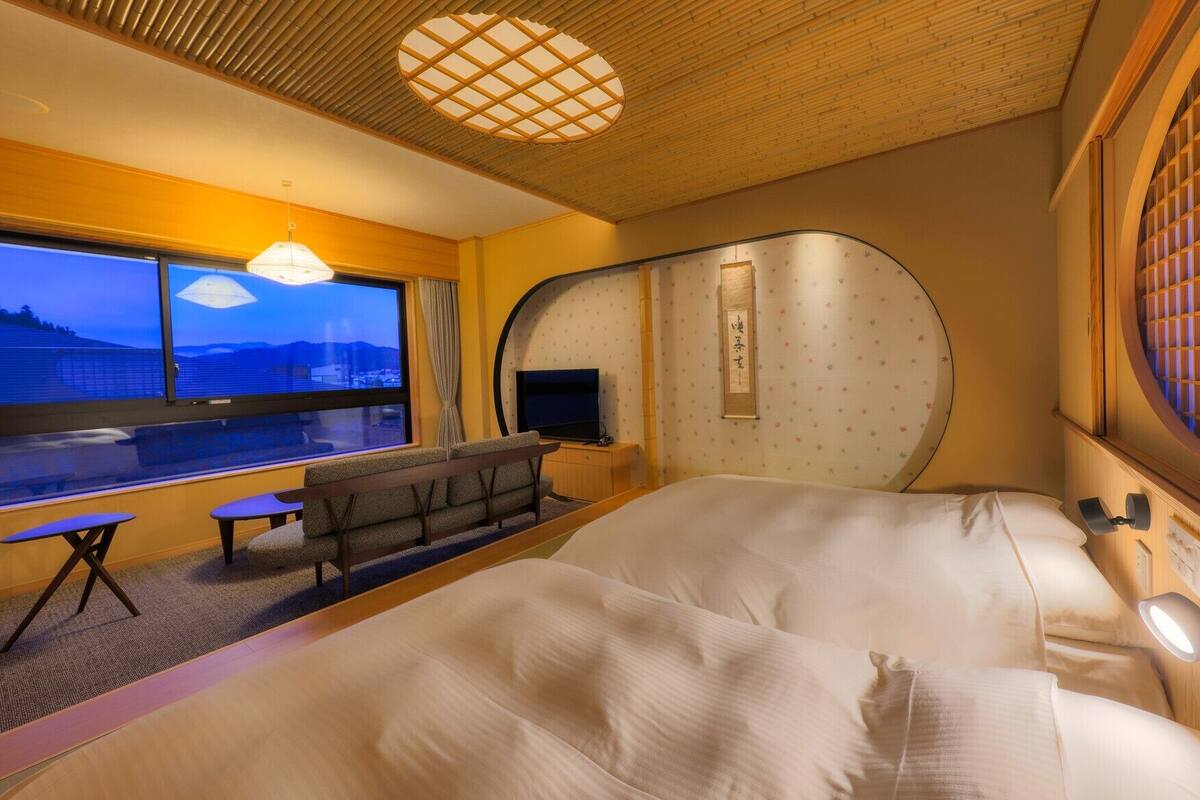 Habitación de hotel con cama, escritorio, silla, televisor, ventana y vista decorativa.