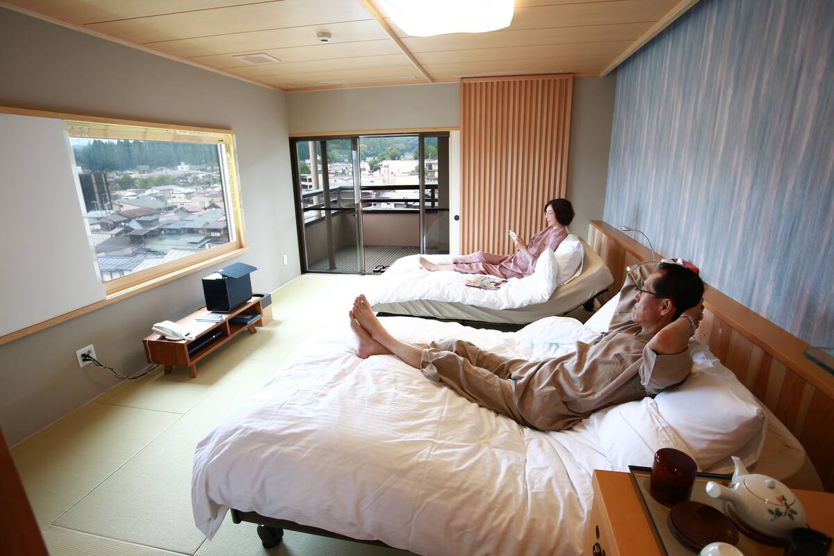 Habitación de hotel con dos camas, vista de la ciudad a través de un ventanal grande y un balcón.