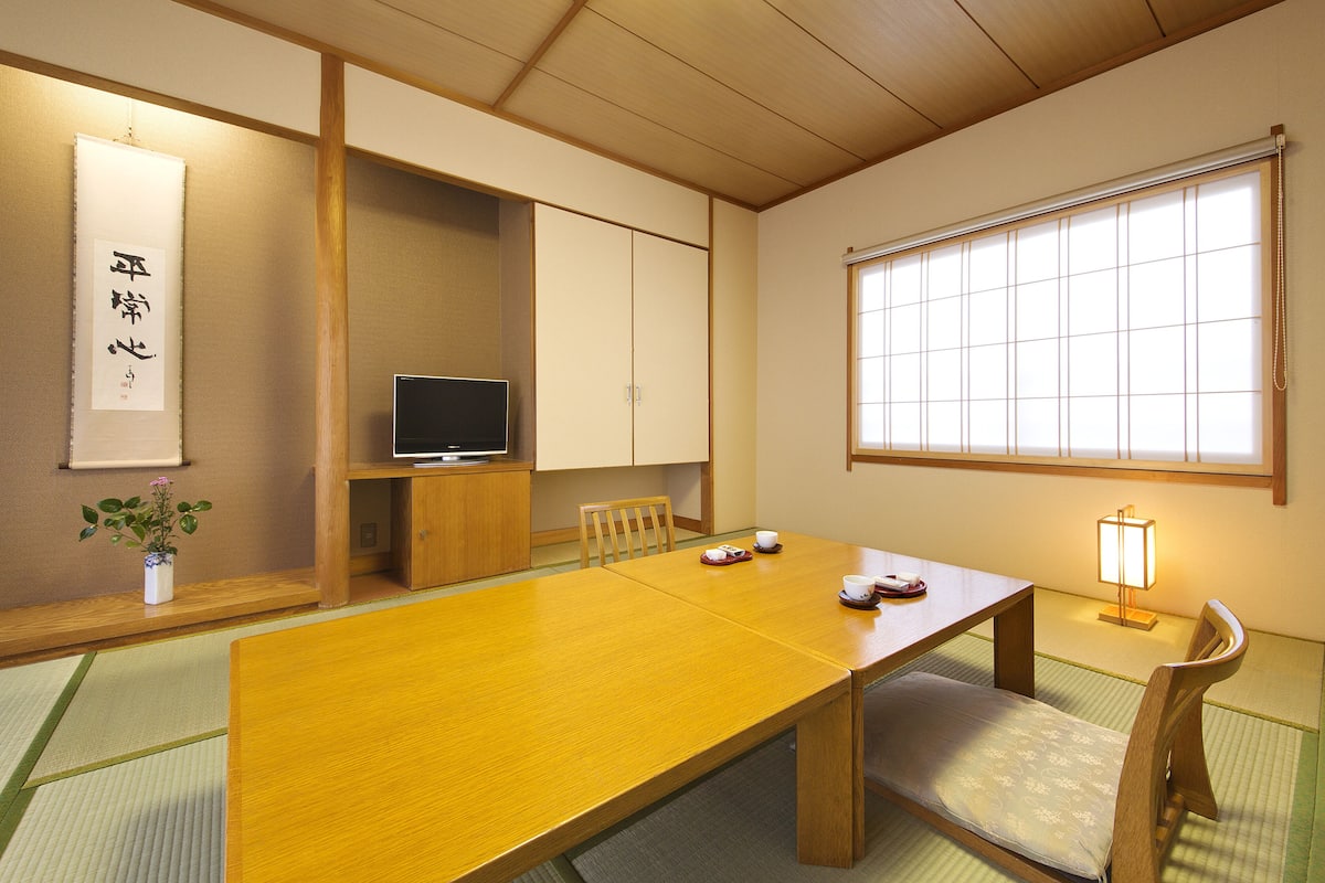 Una habitación japonesa tradicional con suelo de tatami, una mesa baja y un televisor.