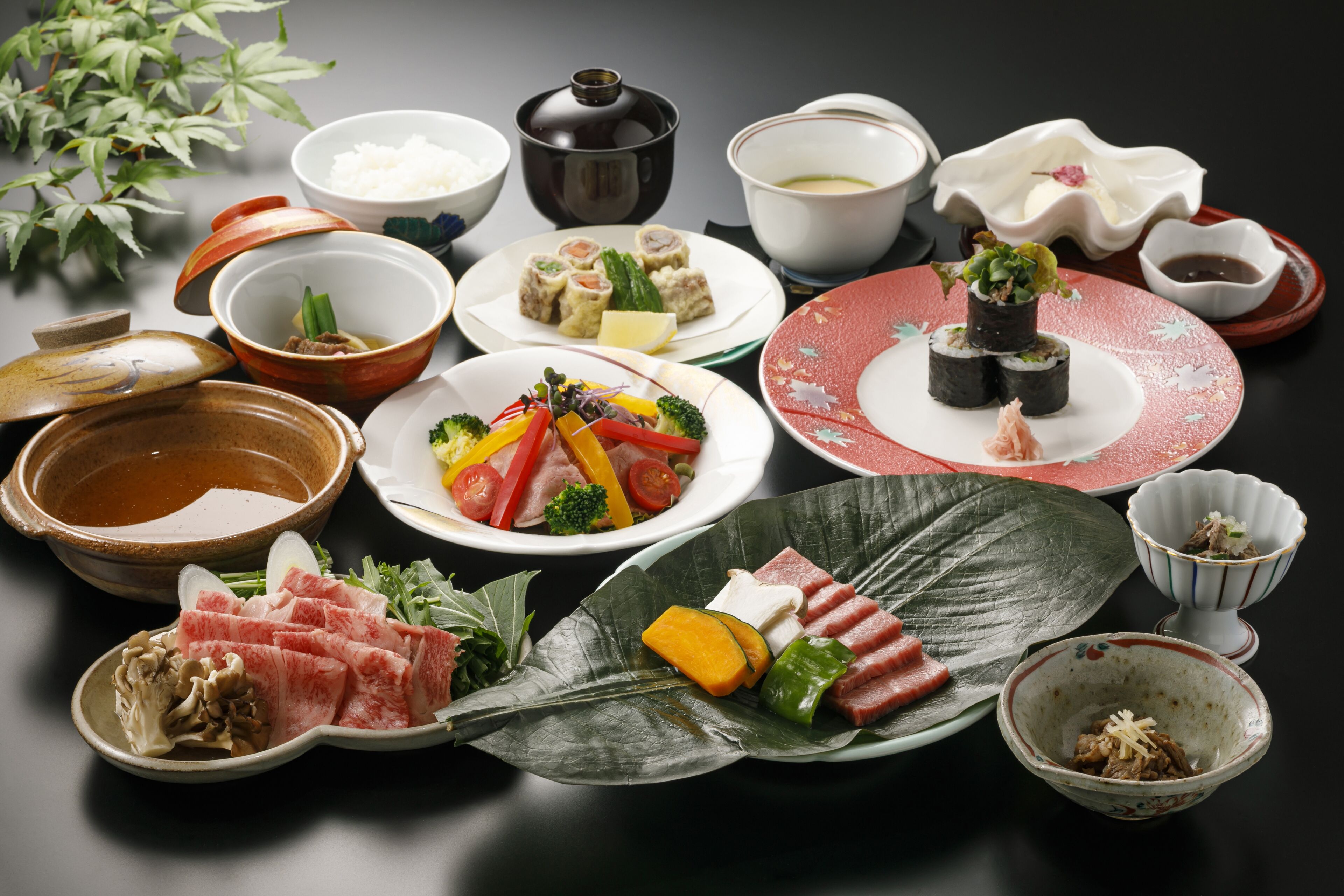 A variety of Japanese dishes including sushi, sashimi, and vegetables, arranged on a table with bowls and plates.
