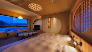 Een moderne hotelkamer met een groot bed, een televisie en uitzicht op een stadsgezicht door grote ramen.