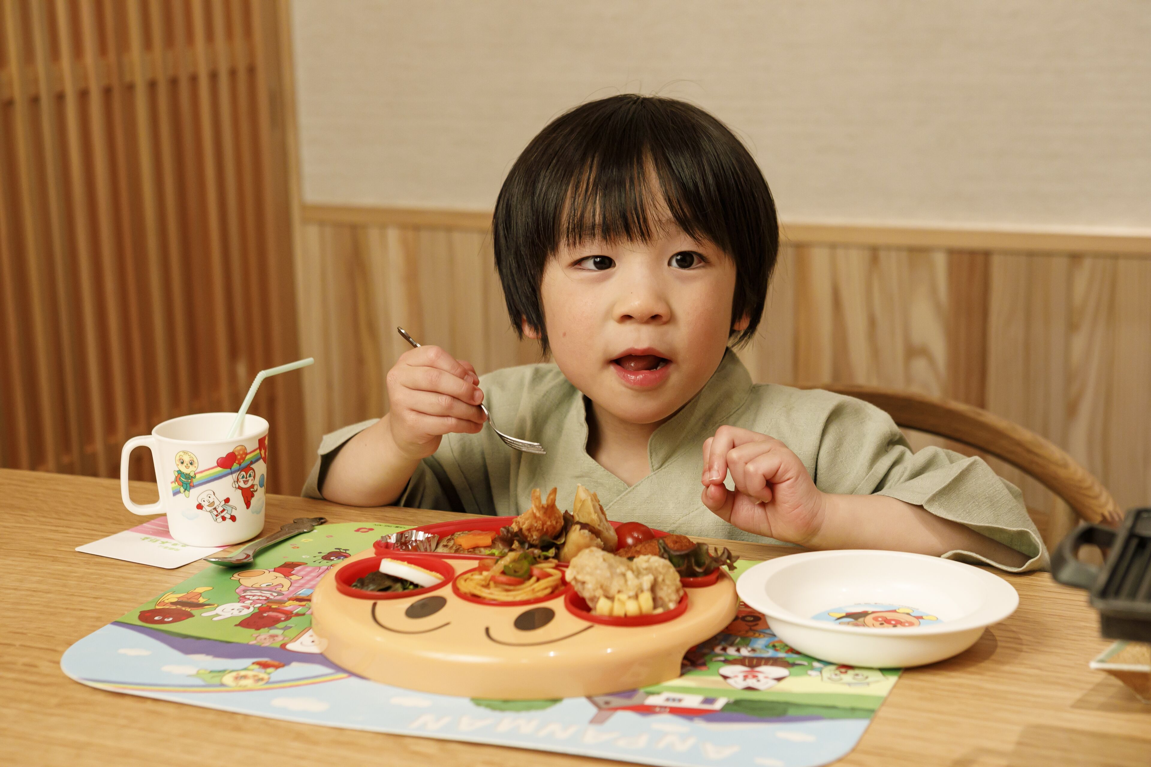 A child sitting at a wooden table with a meal tray, a bowl, and a mug.
