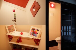 A bathroom with a white toilet, a shelf with decorative items, and a red light on the wall. - Gagakuan (Kyoto)