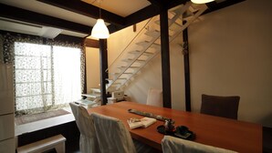A dining area with a wooden table, chairs, a bench, a staircase, and a window with curtains. - Gagakuan (Kyoto)