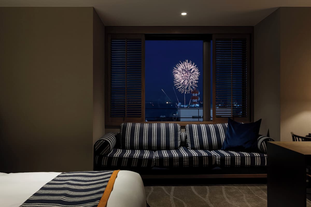 Habitación de hotel con cama, sofá a rayas, mesa de comedor y vistas a fuegos artificiales.