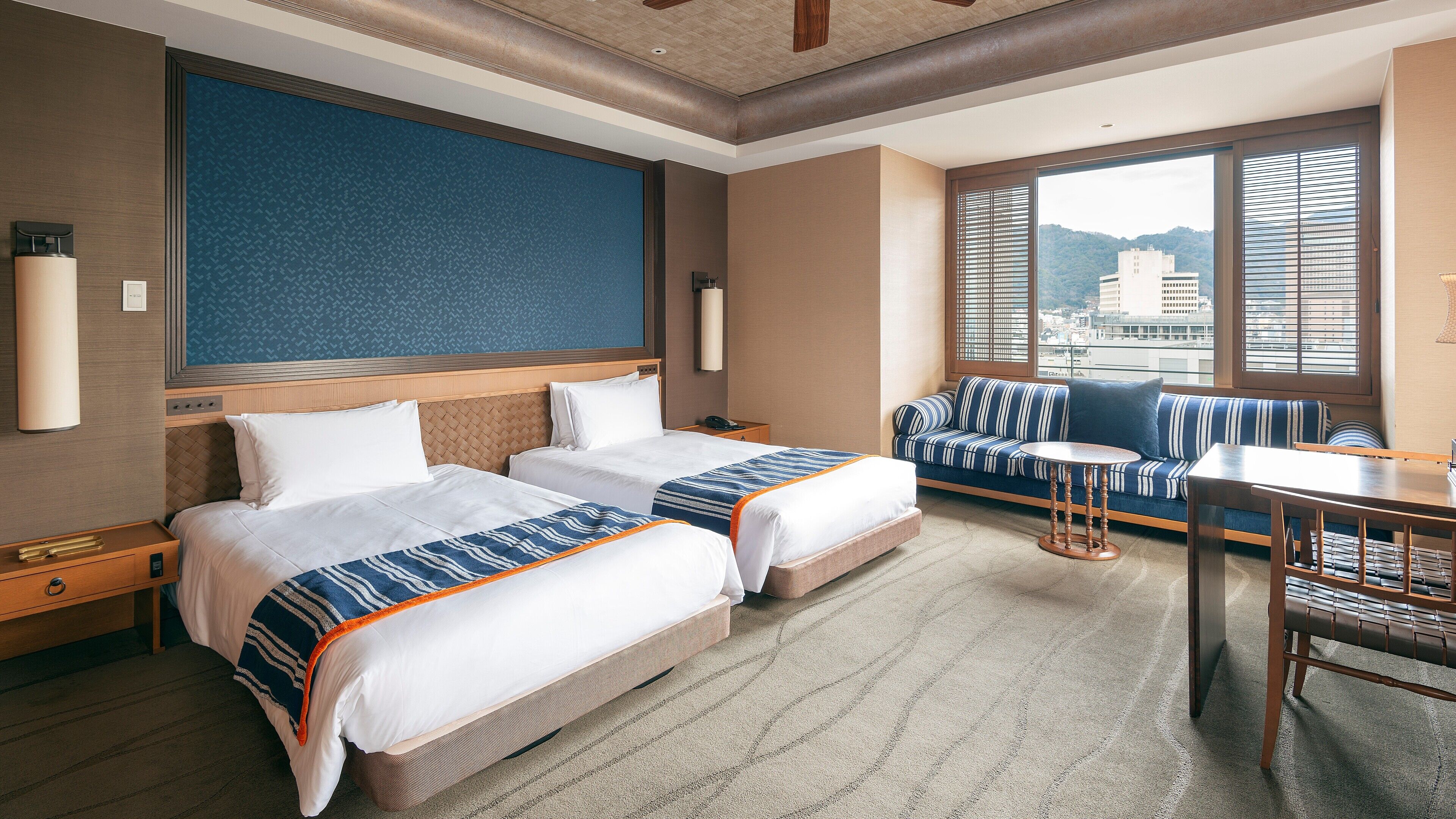 A hotel room with two beds, a sofa, a small table, and a view of the city.