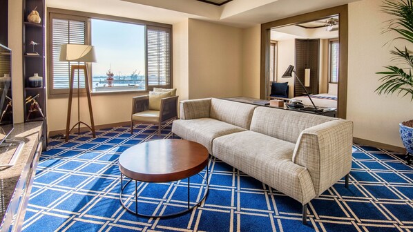 A room with a sofa, a round table, and a view of the outside through large windows.