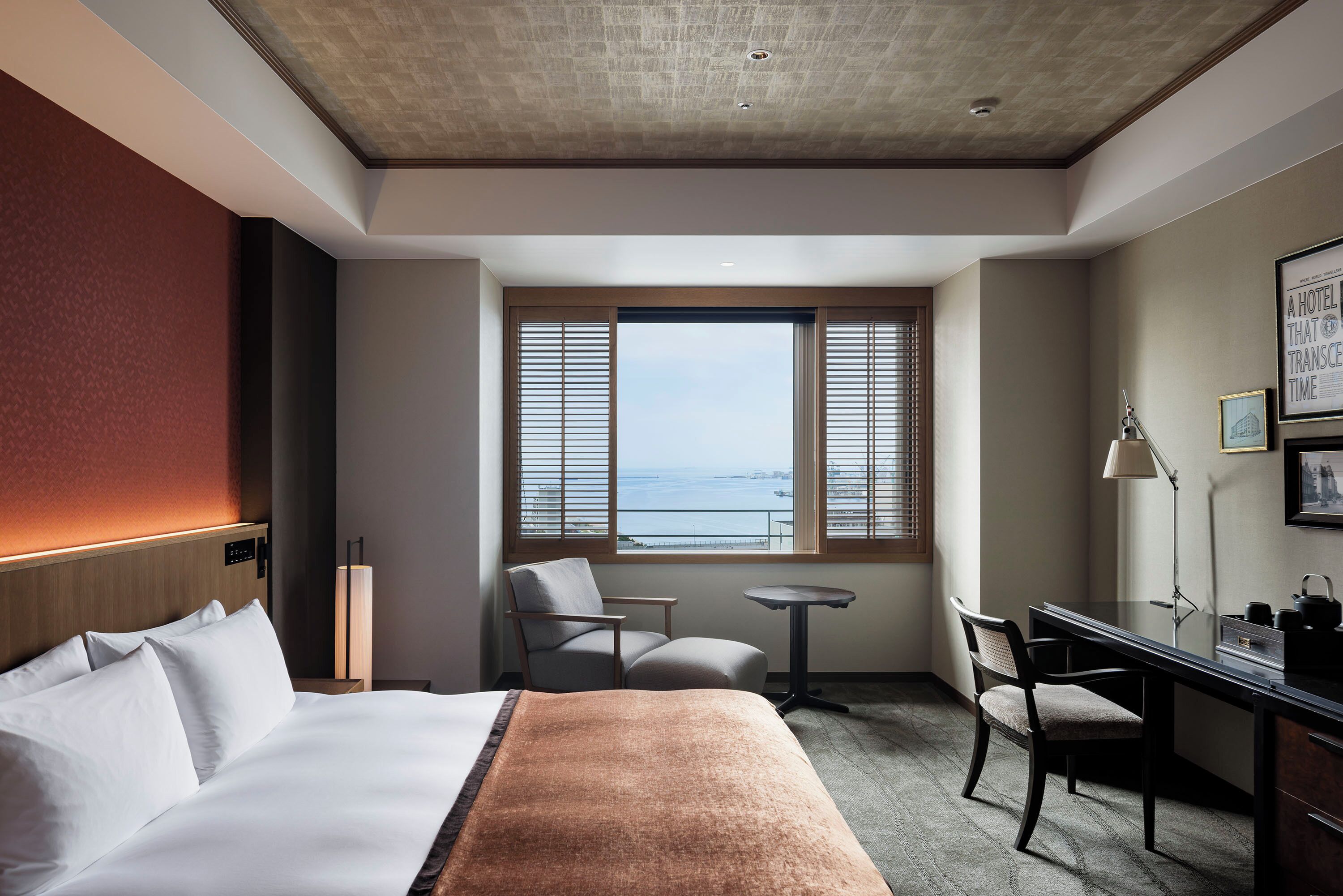 A hotel room with a bed, a desk, a chair, a small table, and a window with a view.