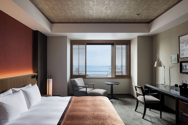 A hotel room with a bed, a desk, a chair, a small table, and a window with a view. - THE ORIENT (Kobe)