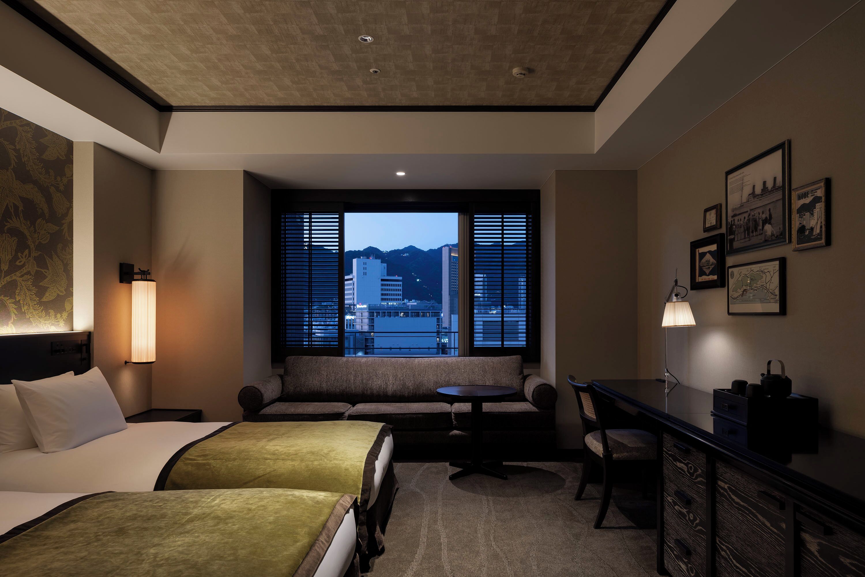 Habitación de hotel con cama, sofá, escritorio y vista a un paisaje urbano.