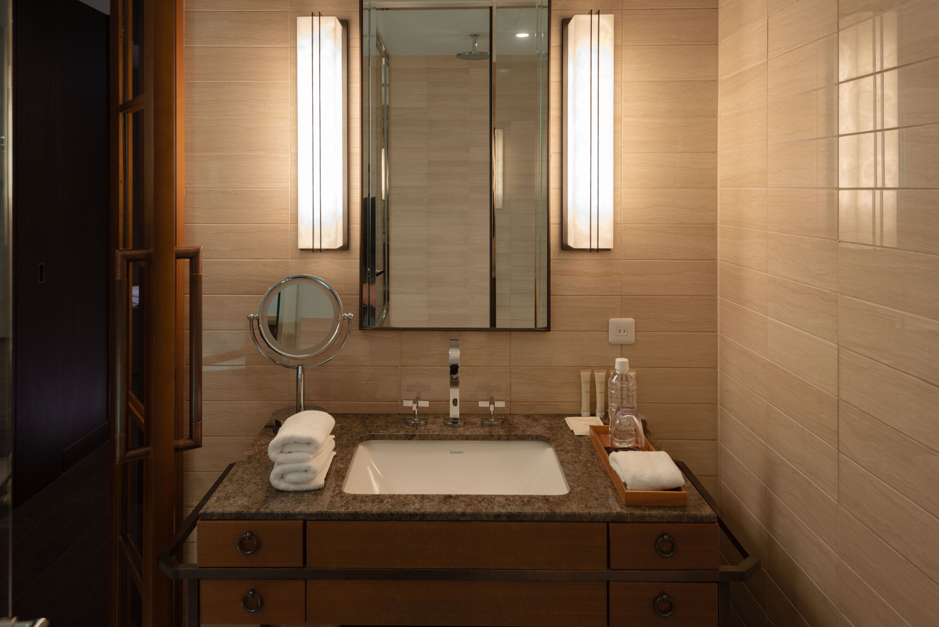 A modern bathroom with a large mirror, a sink, and two wall-mounted lights.