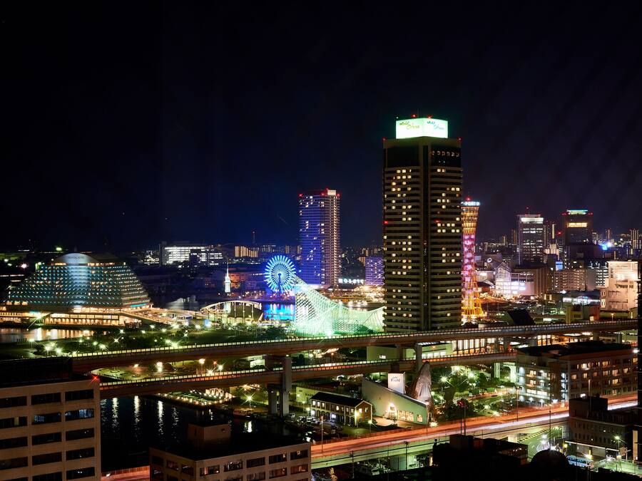 A nighttime cityscape with illuminated buildings, a Ferris wheel, and a prominent tower.