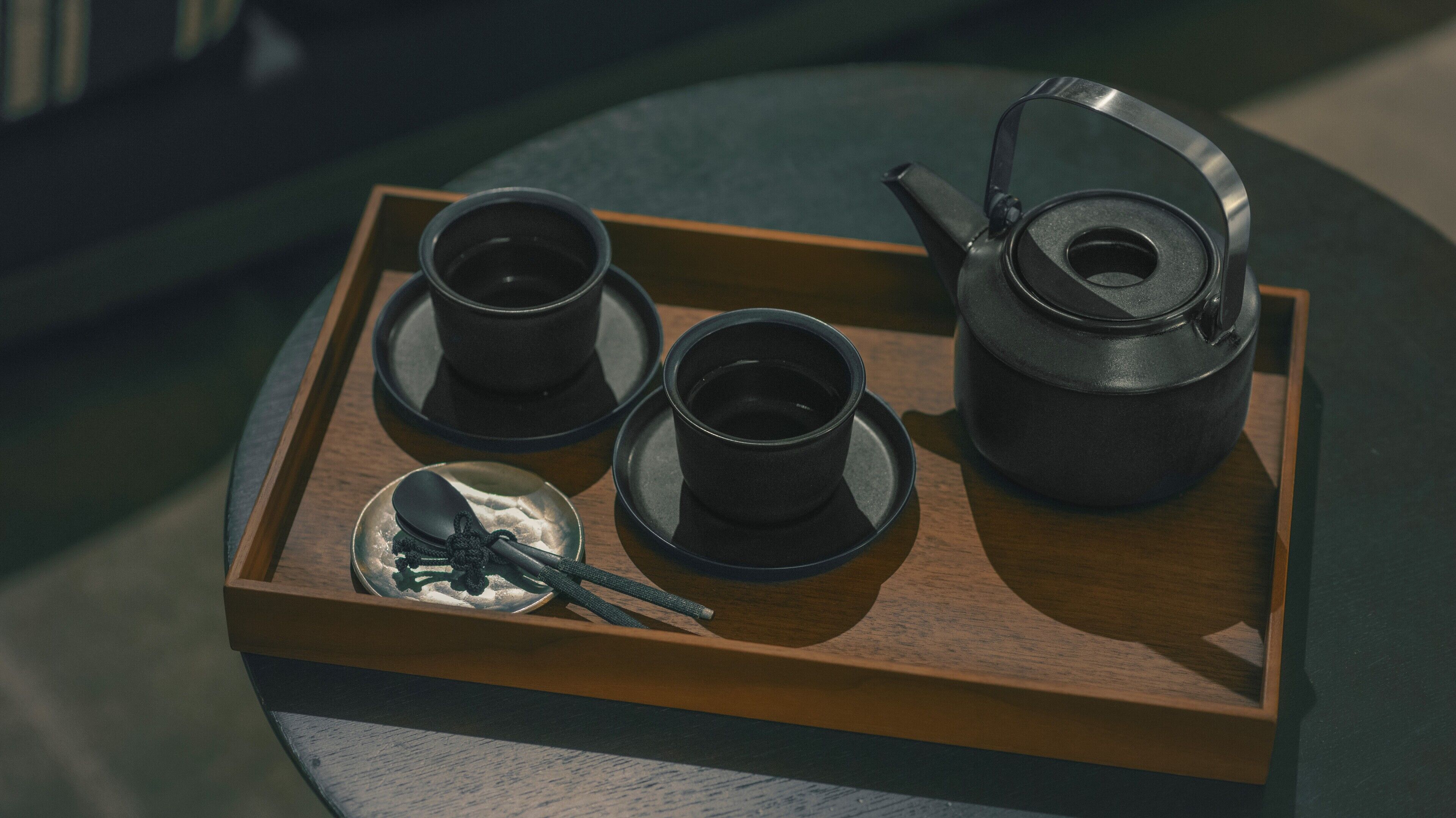 A tray with a teapot, two cups, and a spoon on a wooden surface.