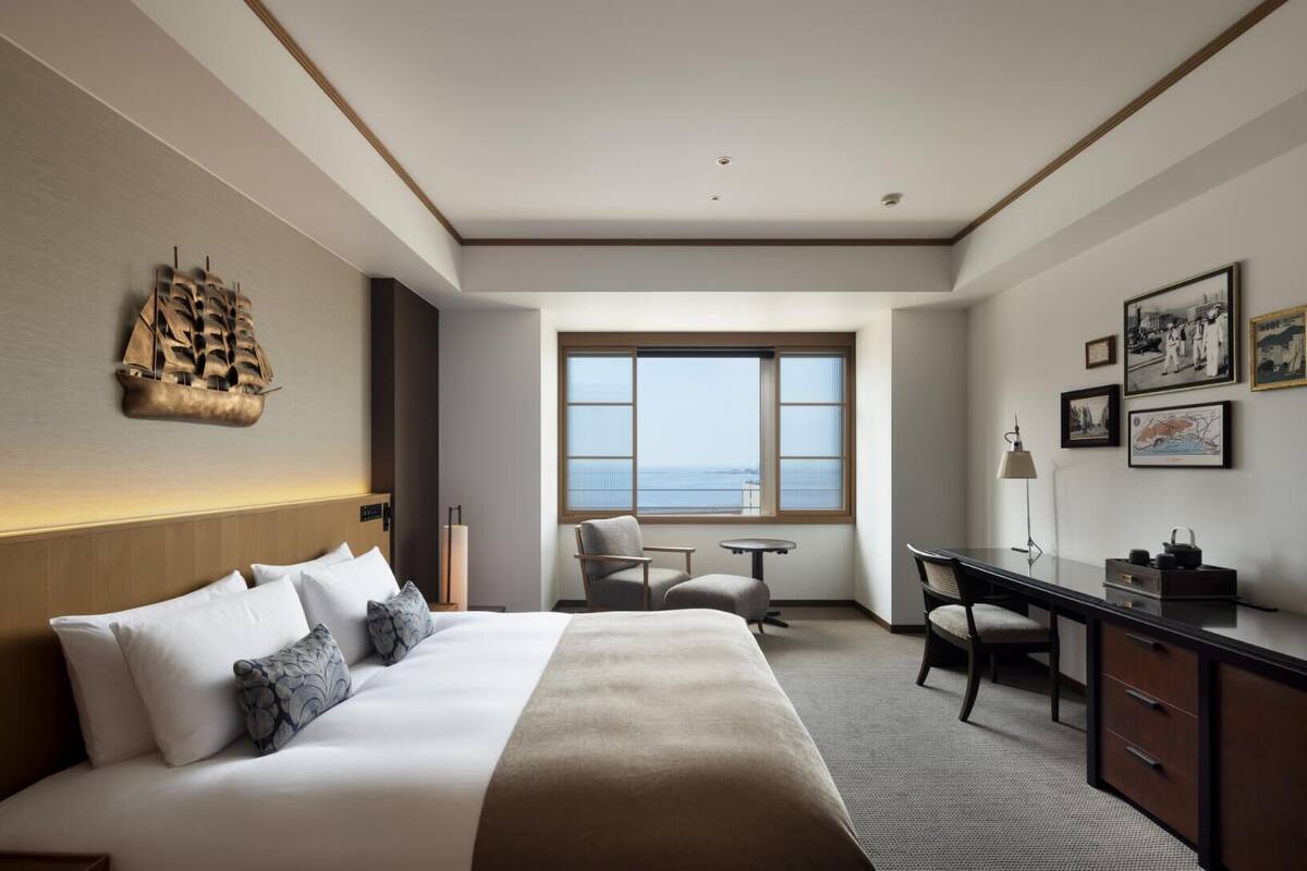 Habitación de hotel con cama, escritorio, sillas, un amplio ventanal con vistas y decoración en la pared.