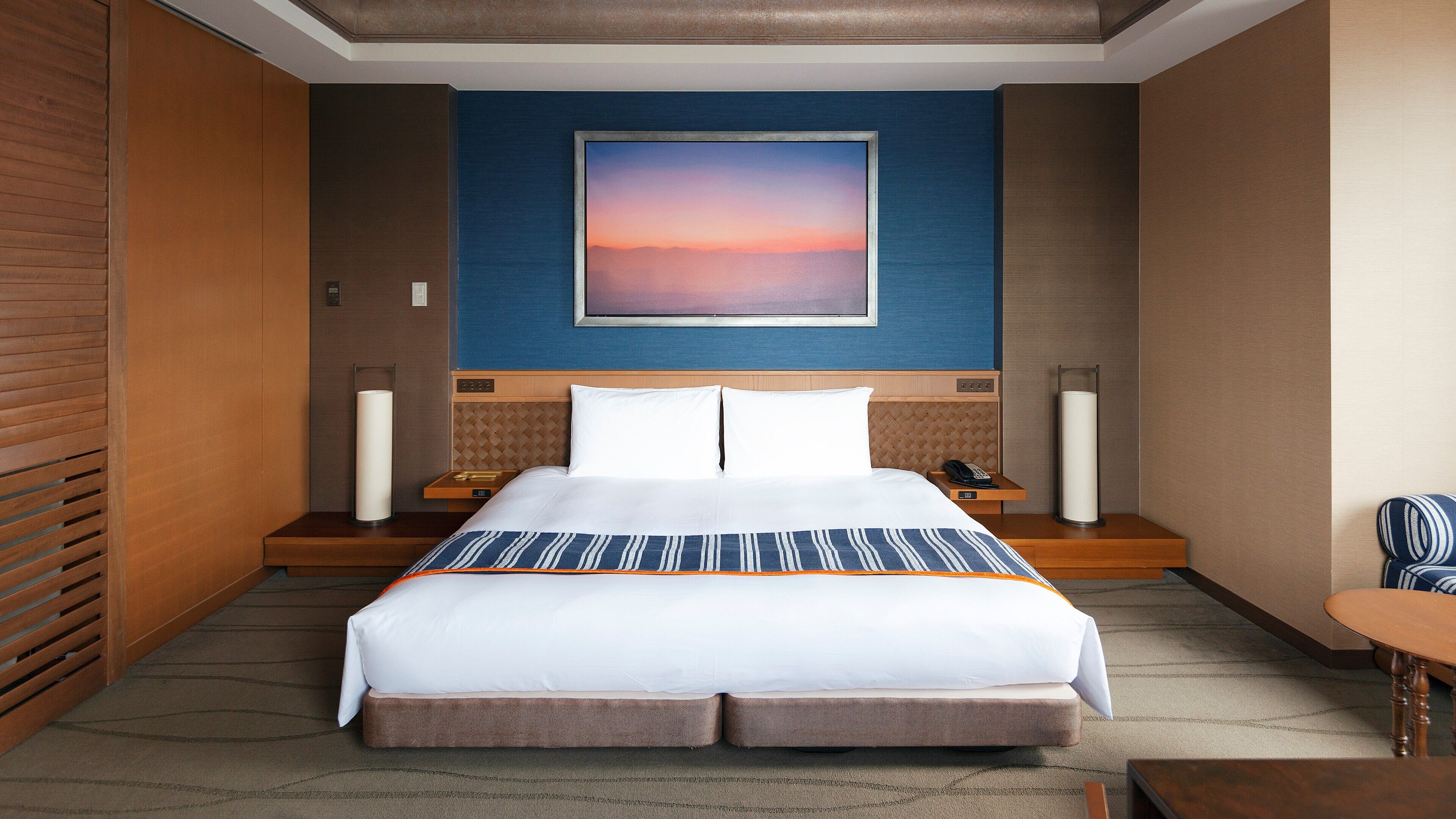 A hotel room with a large bed, a nightstand with a lamp, a telephone, and a chair.