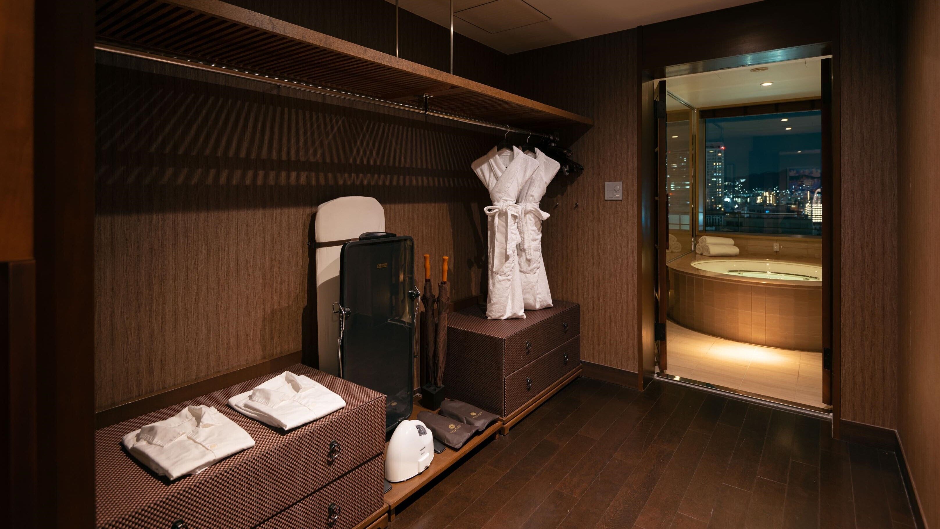 A modern spa room with a wooden floor, a massage table, a massage chair, a sauna, and a view of the city at night.