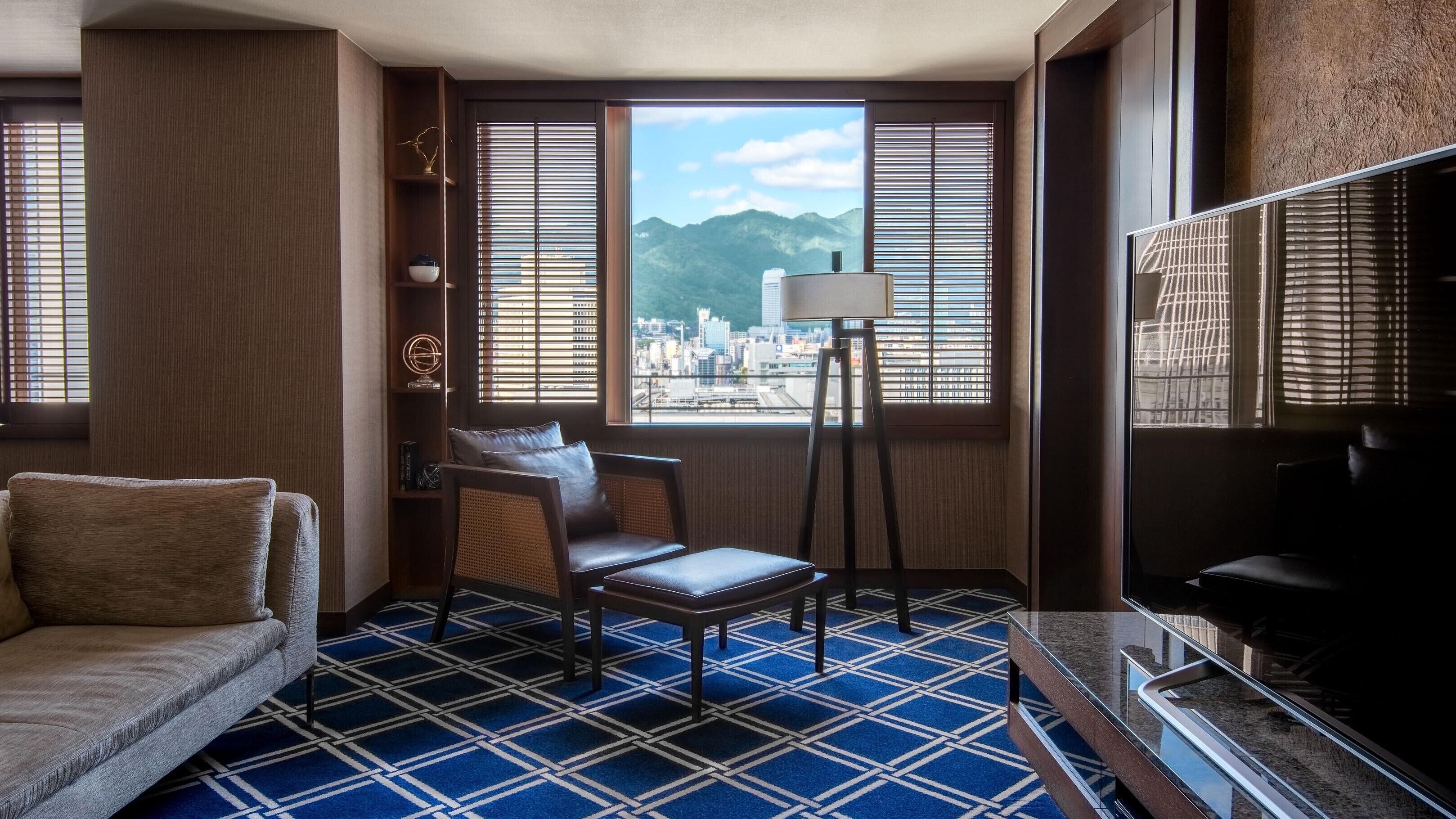A hotel room with a sofa, a chair, a floor lamp, and a TV.