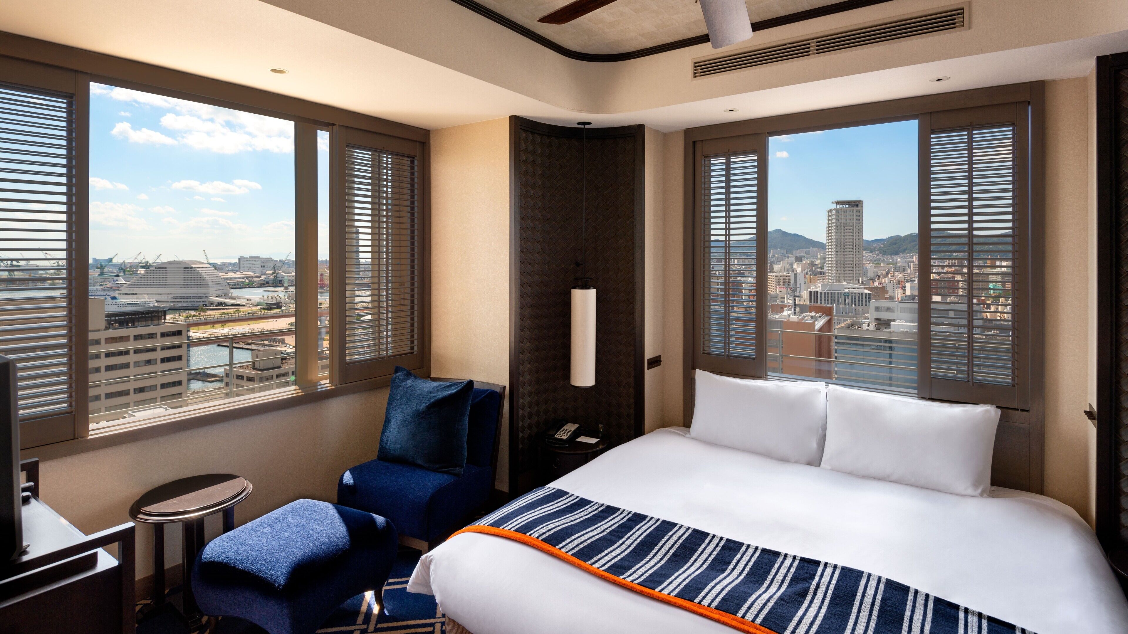 A hotel room with a large bed, a desk, a chair, and a view of the cityscape.