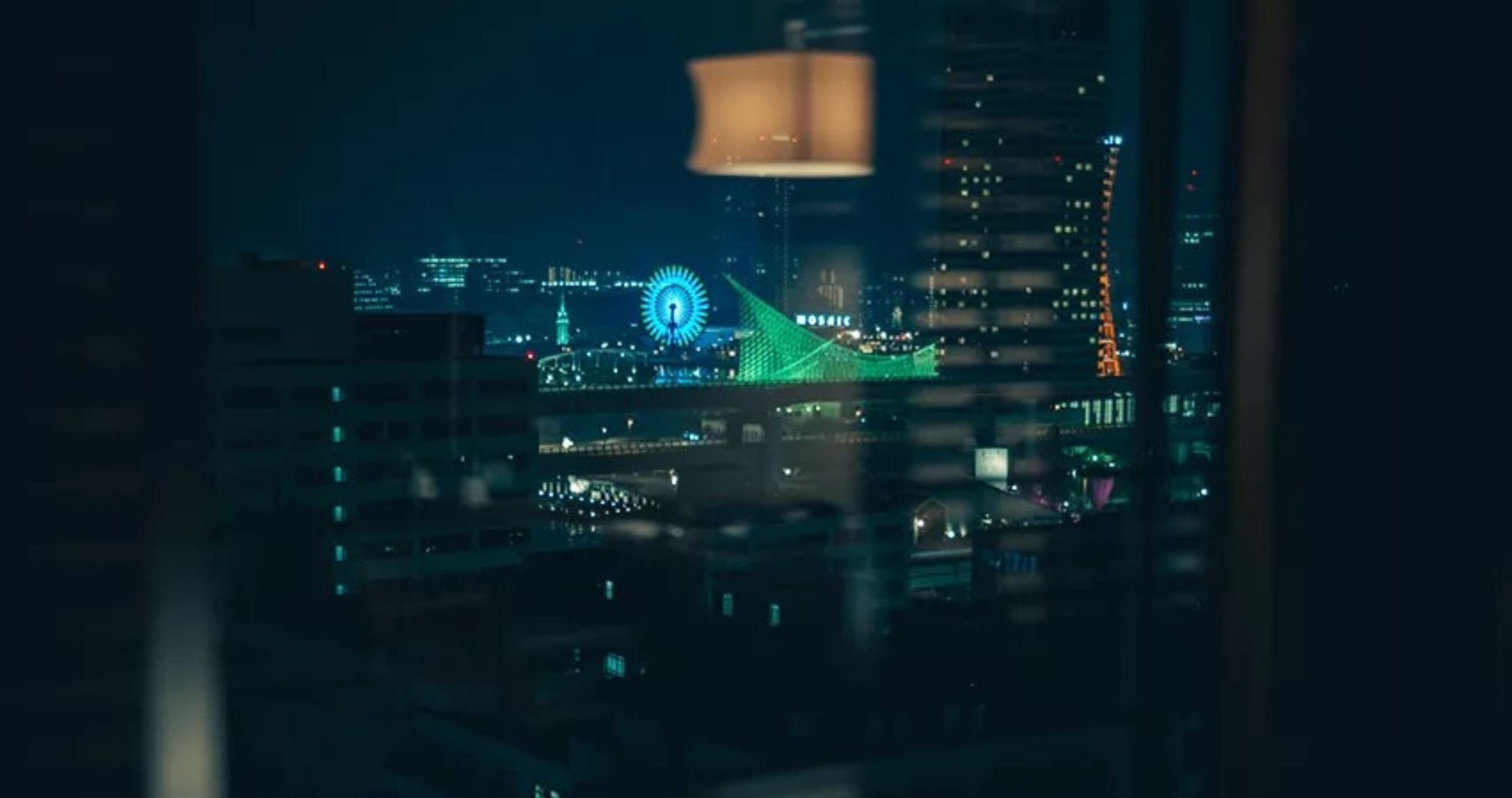 Un paisaje urbano nocturno con una noria destacada y un puente iluminado en verde.