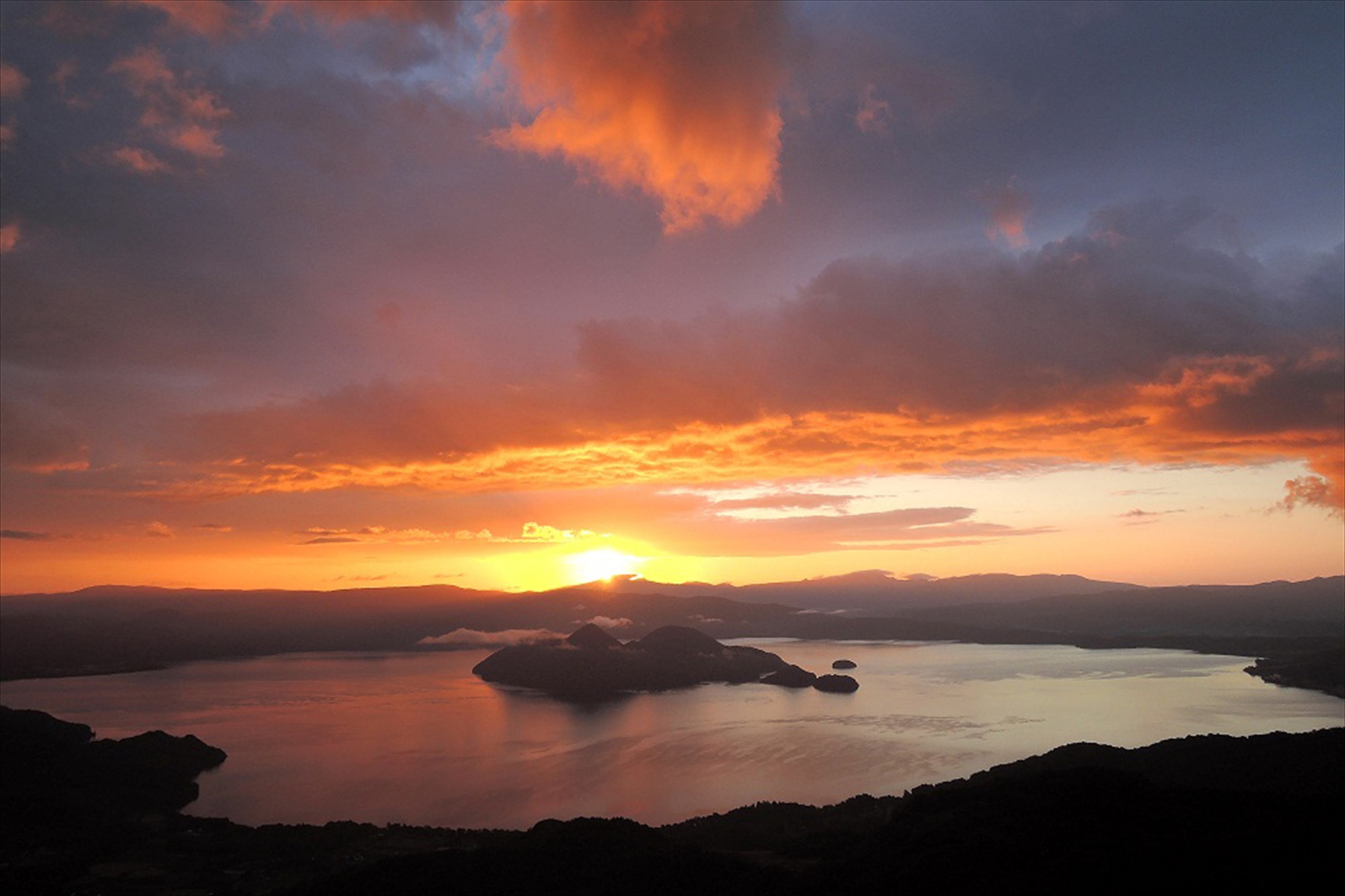 A sunset over a calm lake with distant landforms.