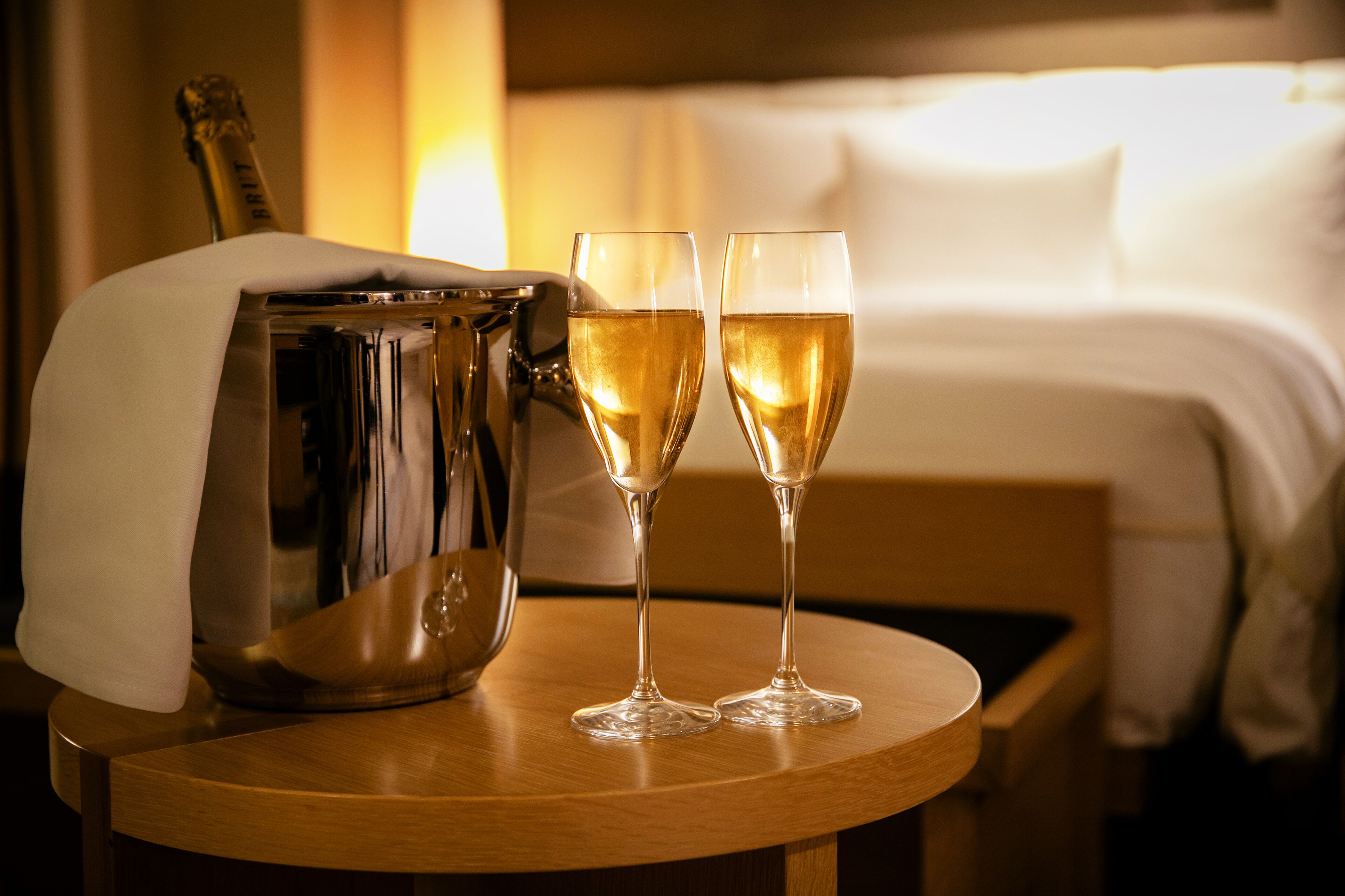 A bed, a bedside table with a champagne bucket and two glasses of champagne.