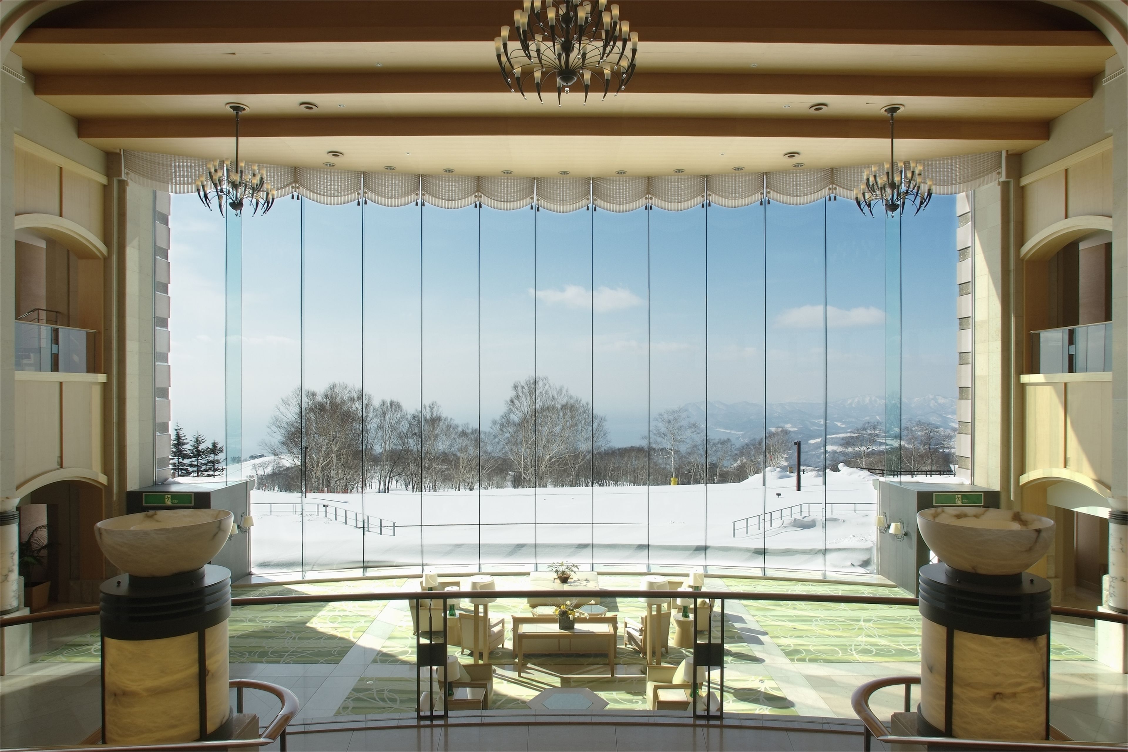 A spacious room with a large window, a chandelier, and a view of a snowy landscape.