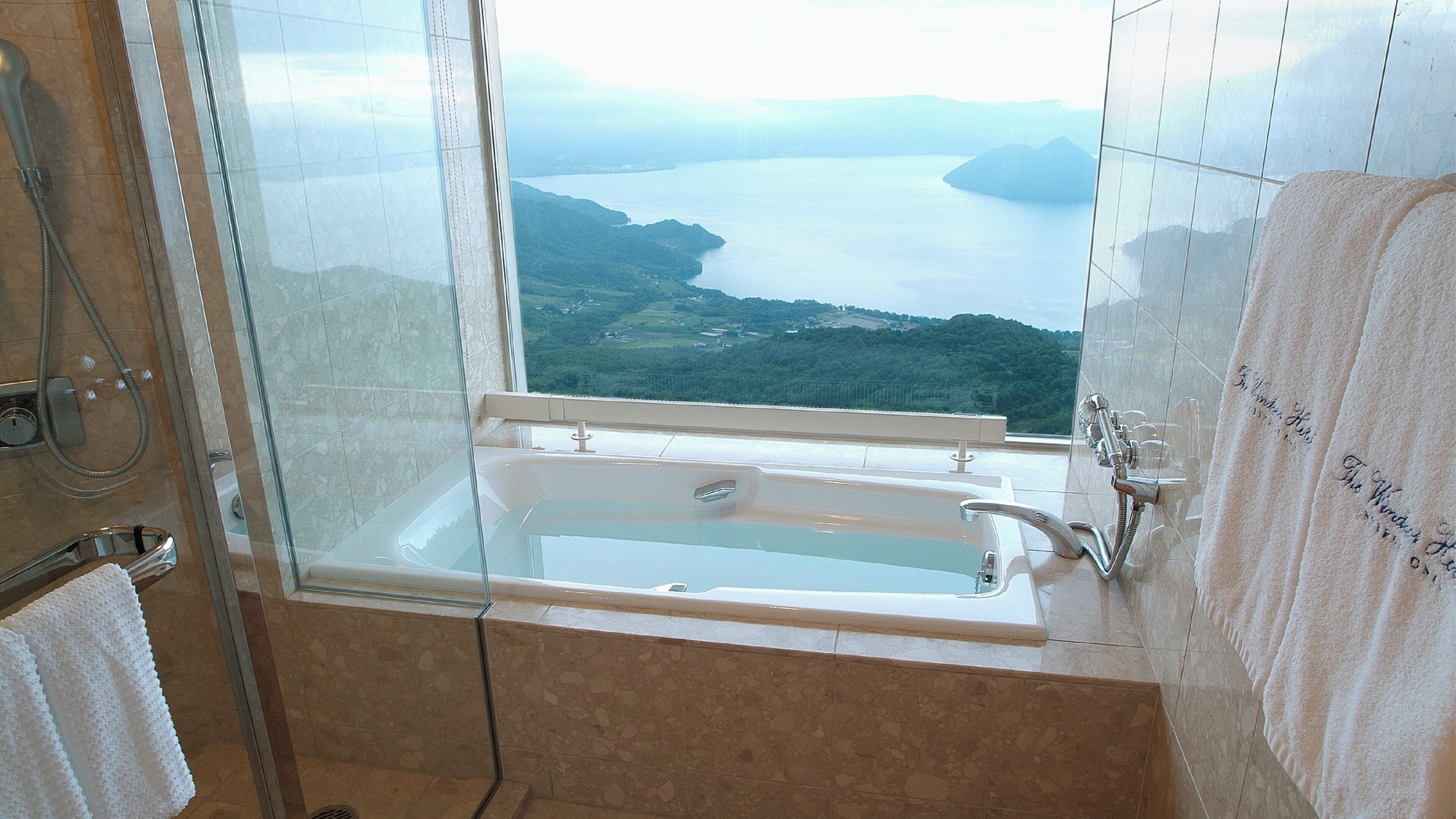 Un baño con bañera y ducha, vistas a un lago y montañas, y un perchero con toallas.