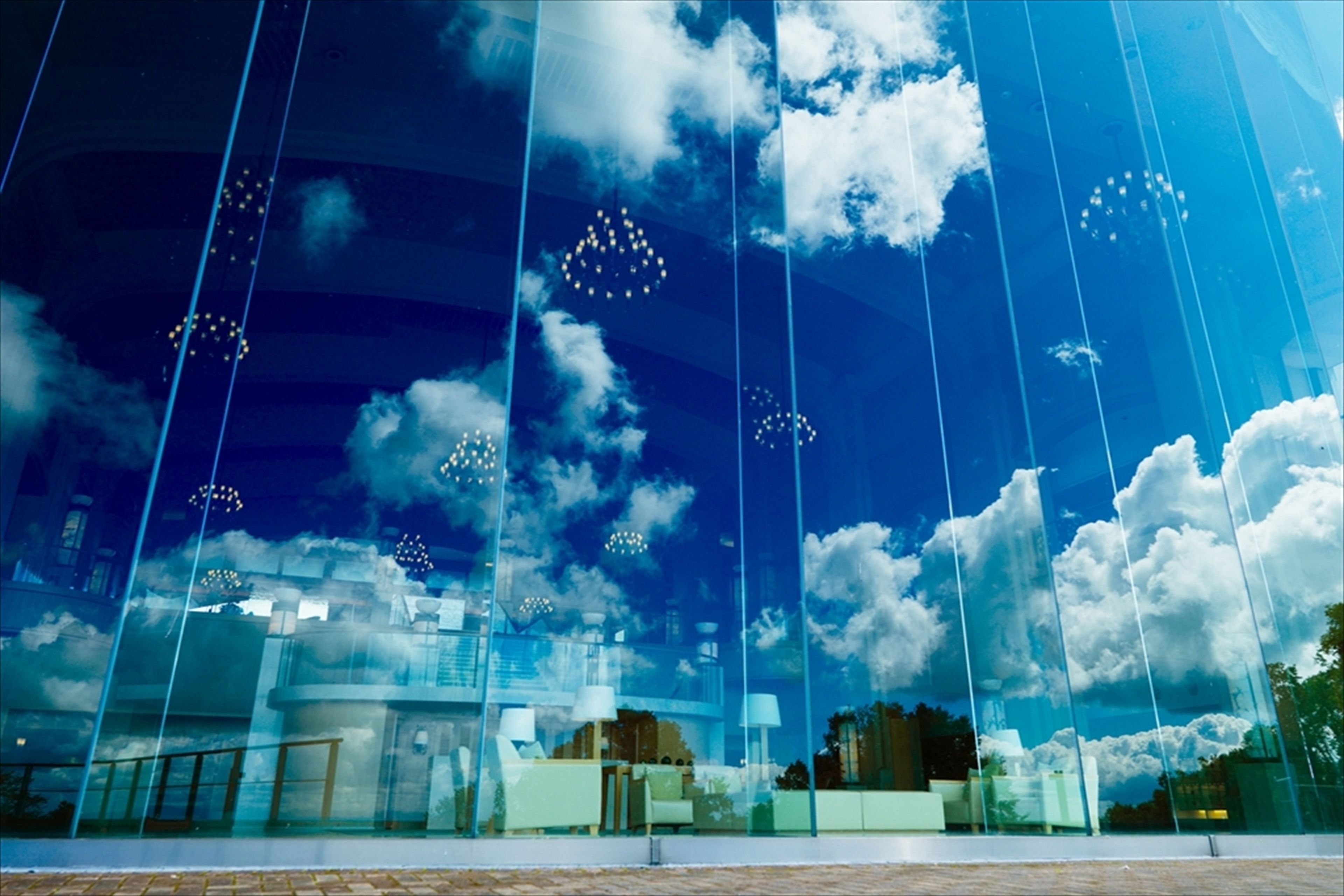 A modern building with large glass windows reflecting clouds and sky.