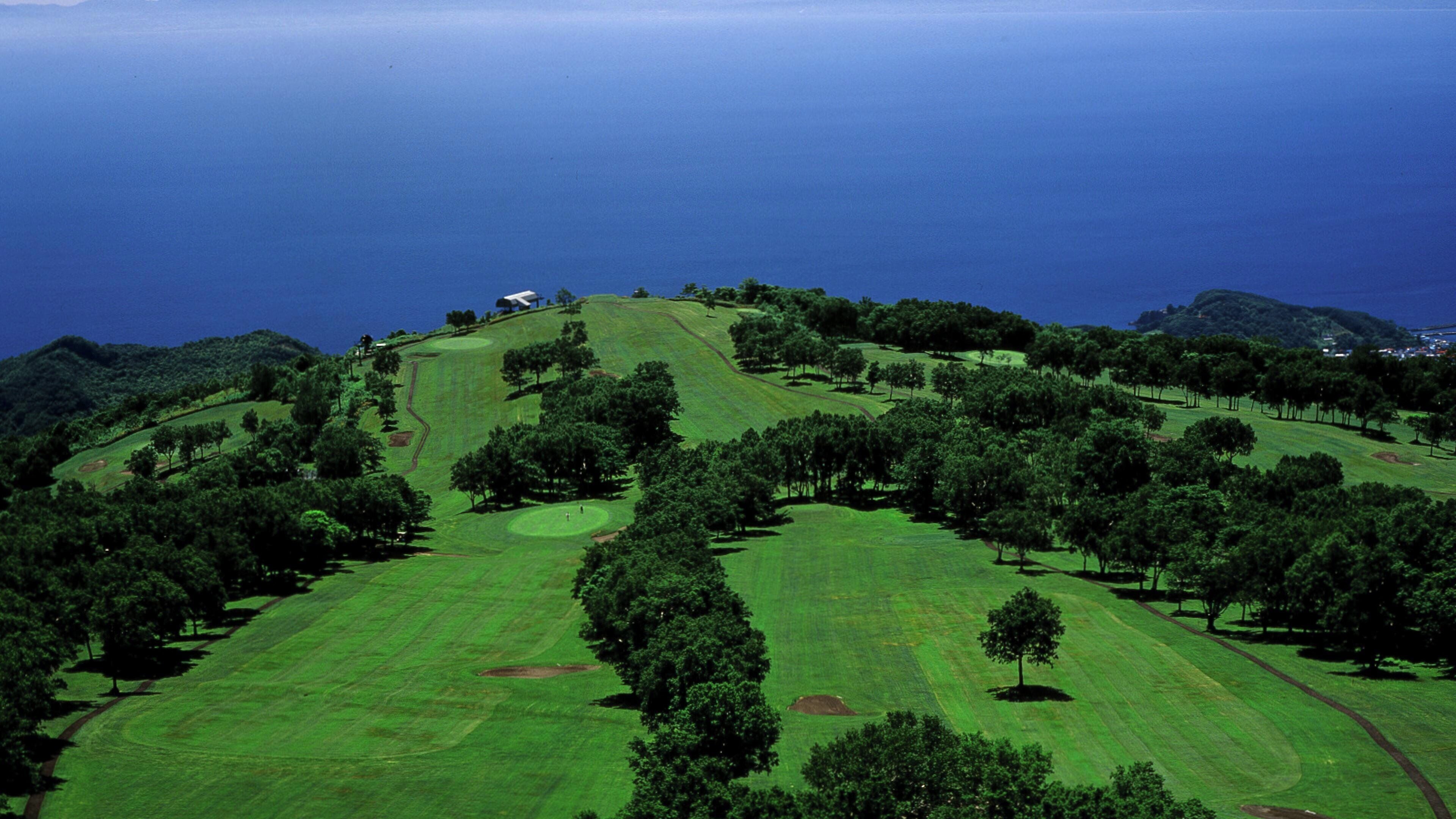 Un campo de golf con vistas al océano y colinas.