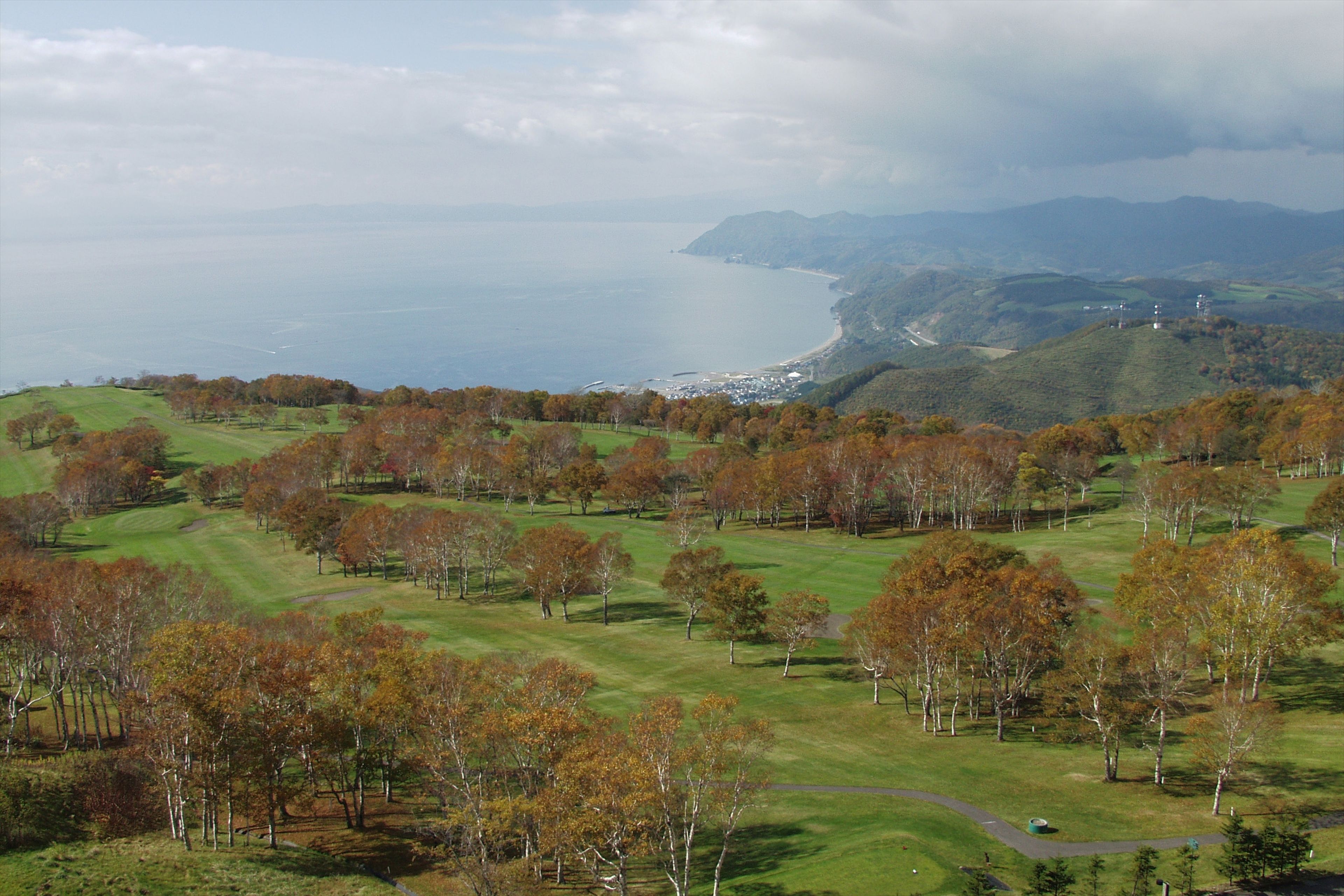 Vista panorámica de un paisaje costero con colinas ondulantes, una playa y cielo despejado.