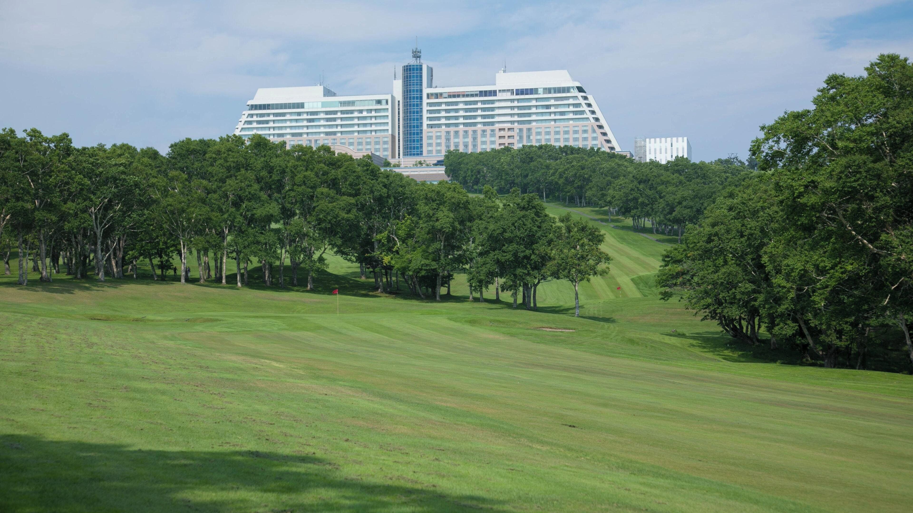 A golf course with a large hotel in the background.
