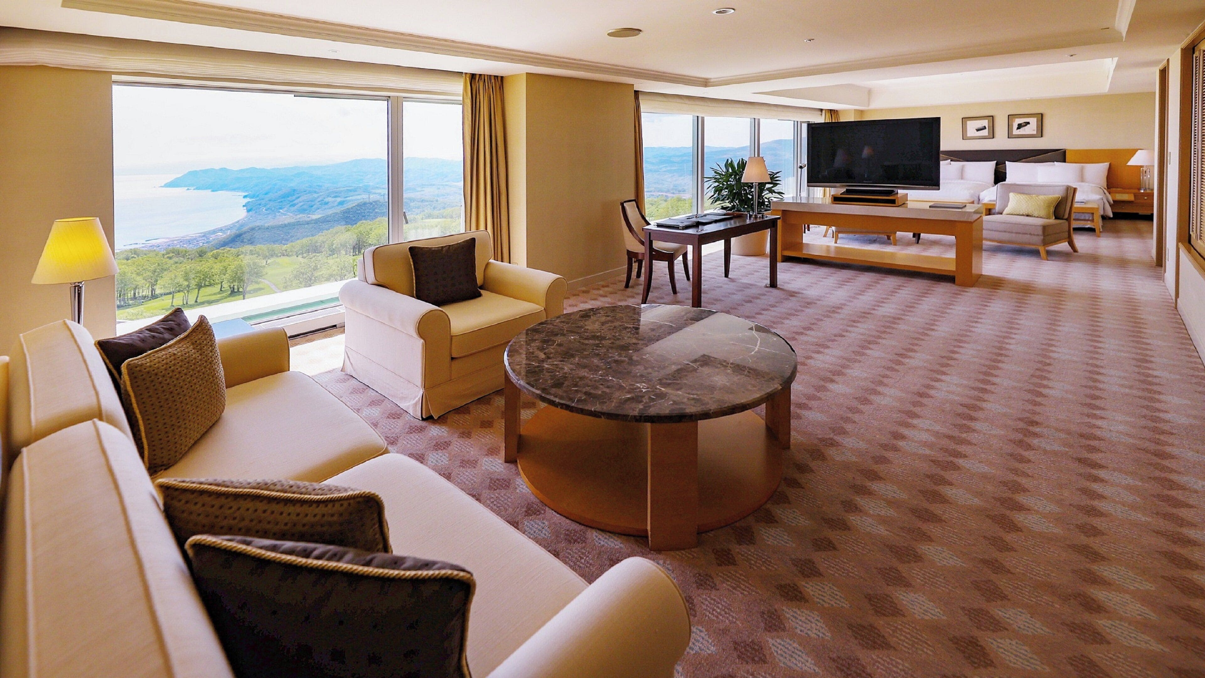 Un salón espacioso con un amplio ventanal que ofrece una vista panorámica, un sofá cómodo, una mesa de centro y un televisor de pantalla plana.
