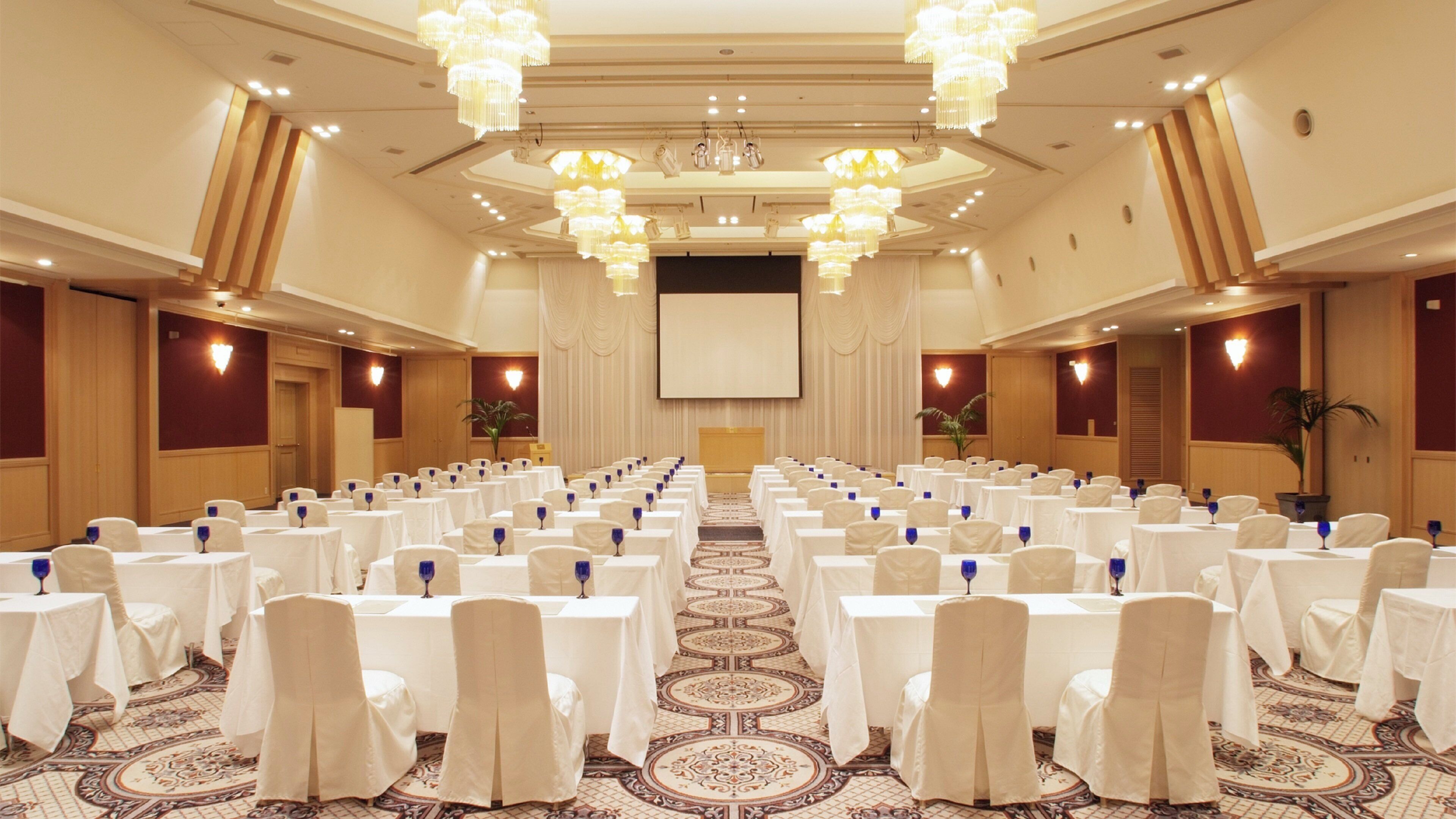Un salón de conferencias con filas de mesas, manteles blancos y sillas azules.