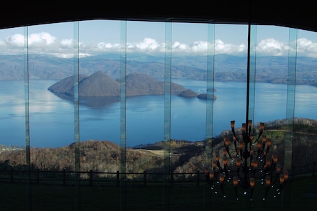 A panoramic view through a curved window, featuring a lake surrounded by hills and a distant mountain range.