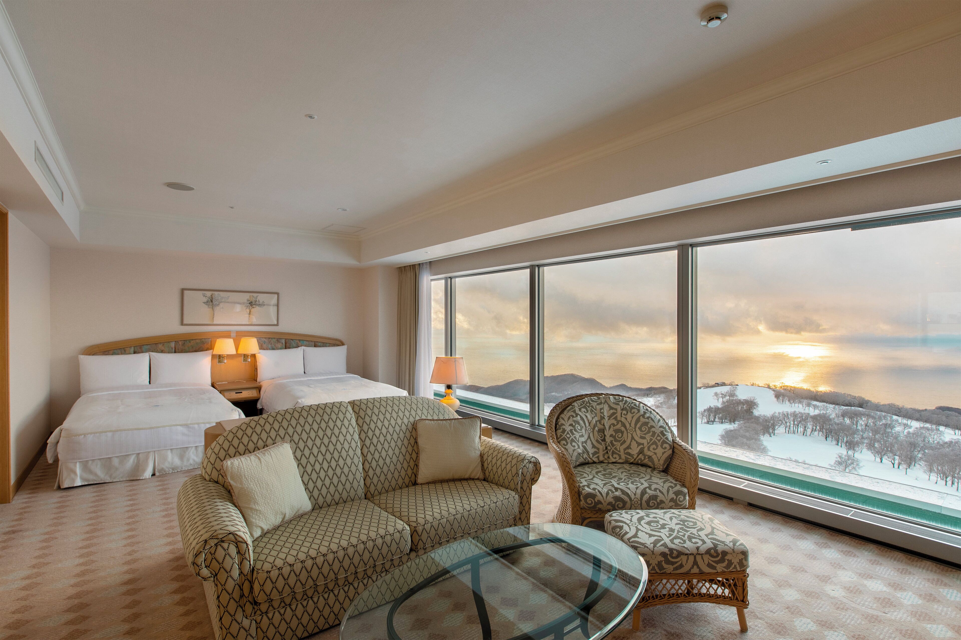 A hotel room with a large bed, two bedside tables, a sofa, a chair, and a glass coffee table.