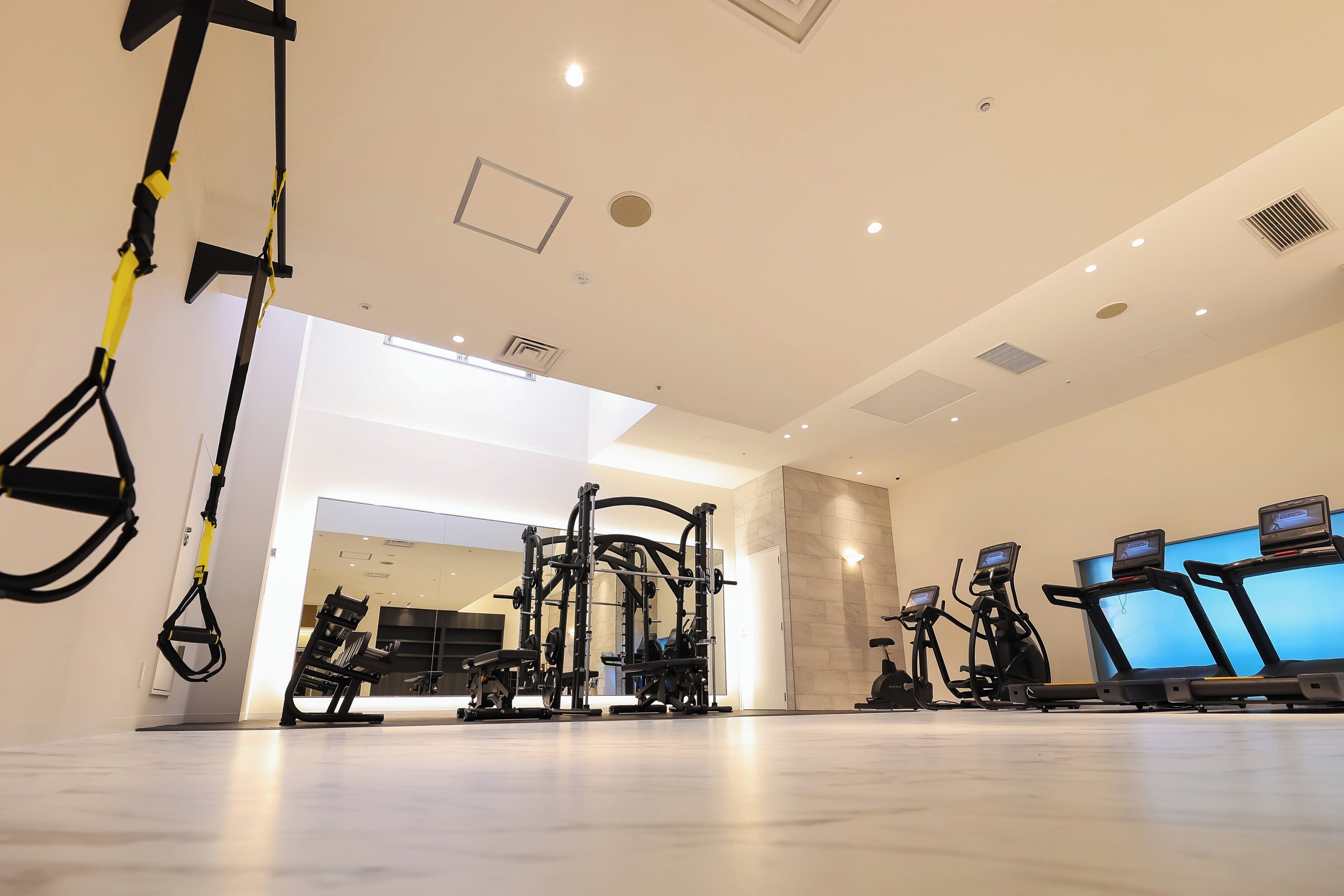 A modern gym with exercise equipment, including TRX straps, a squat rack, and treadmills.