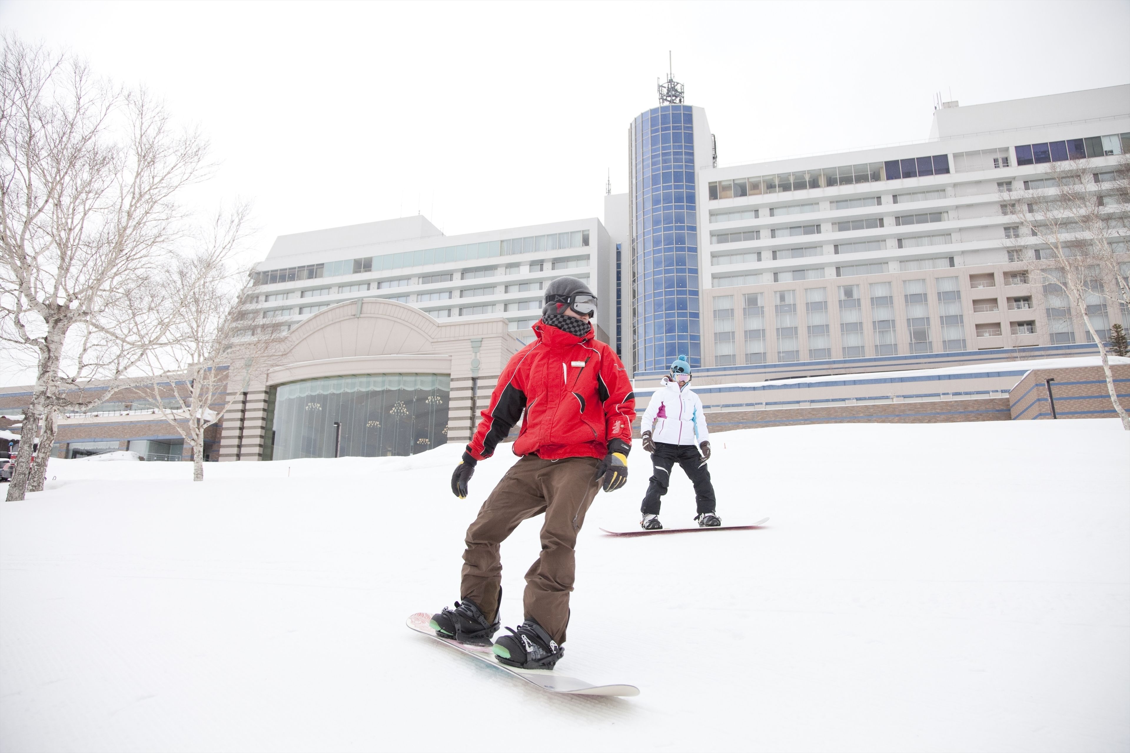 A person snowboarding in a snowy area with buildings in the background.