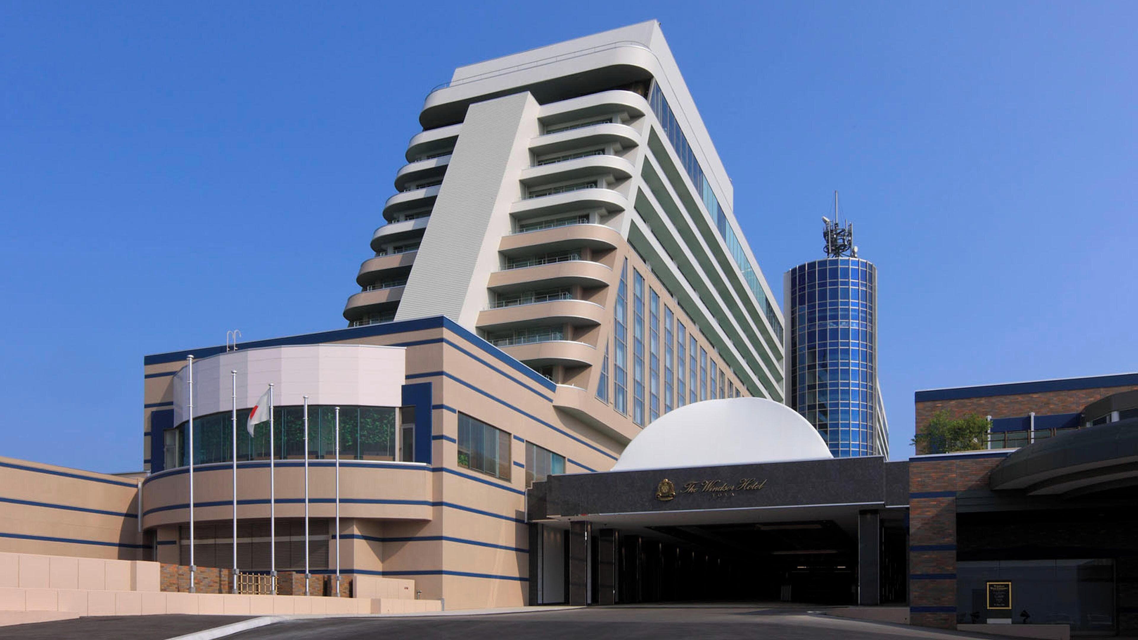 Un hotel moderno con fachada curva, varios balcones y una torre destacada.
