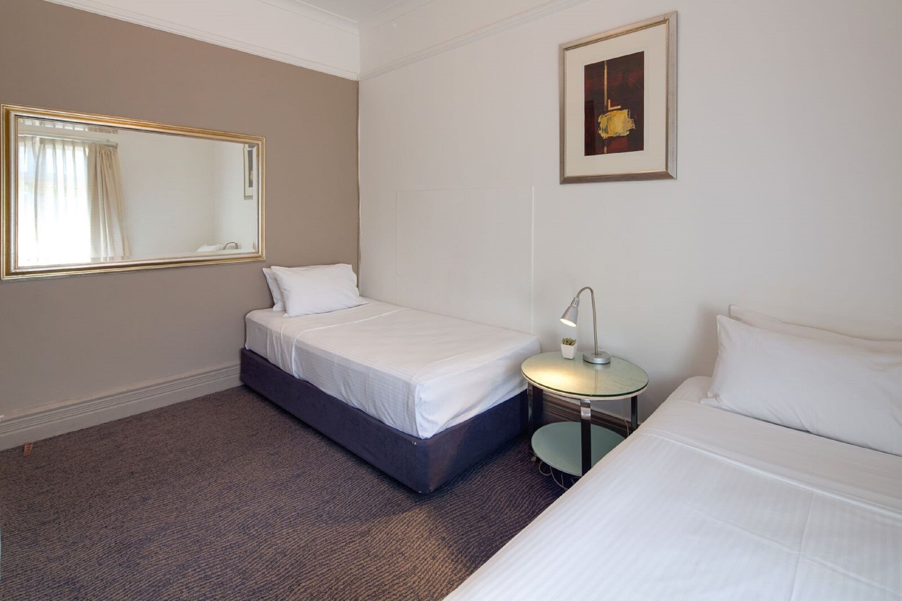 A hotel room with two beds, a round table with a lamp, a large mirror, and a framed picture on the wall.