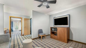 A hotel room with a bed, a TV, a microwave, a chair, and a patterned carpet.