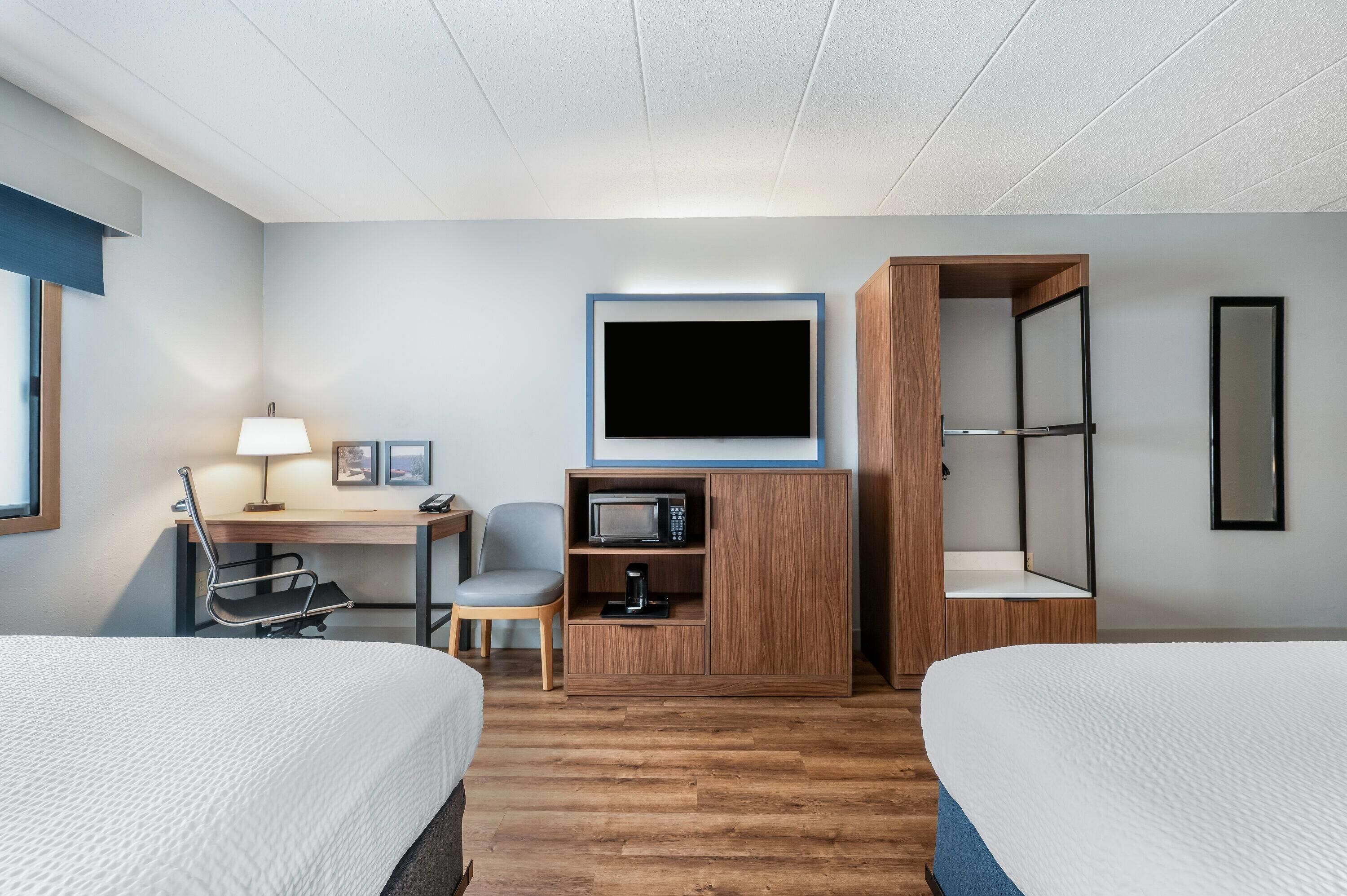 Une chambre d’hôtel avec deux lits, un bureau avec une lampe, une télévision, un four à micro-ondes, une machine à café et une armoire.