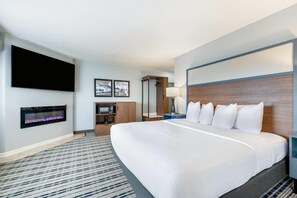 A hotel room with a large bed, a flat-screen TV mounted on the wall, a fireplace, a microwave, and a mirror. - AmericInn by Wyndham Baudette (Baudette)