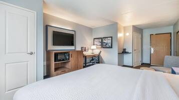 Habitación de hotel con una cama grande, un televisor de pantalla plana montado en la pared, un escritorio con lámpara y una zona de estar con una silla.