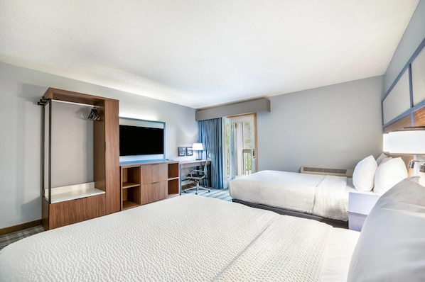 A hotel room with two beds, a TV, a desk, and a window with curtains.