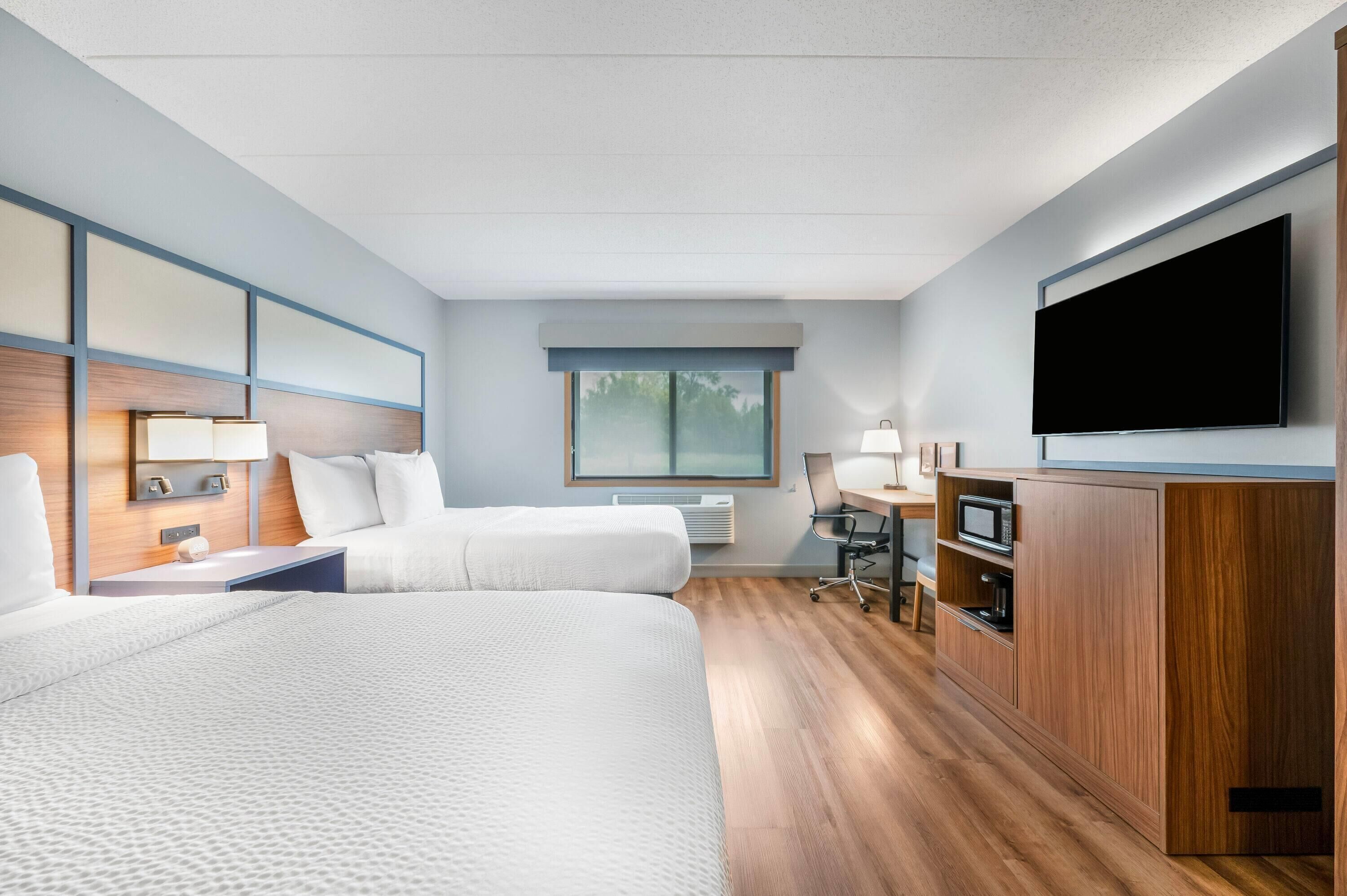 Habitación de hotel con dos camas, televisión, escritorio con silla, microondas y armario.