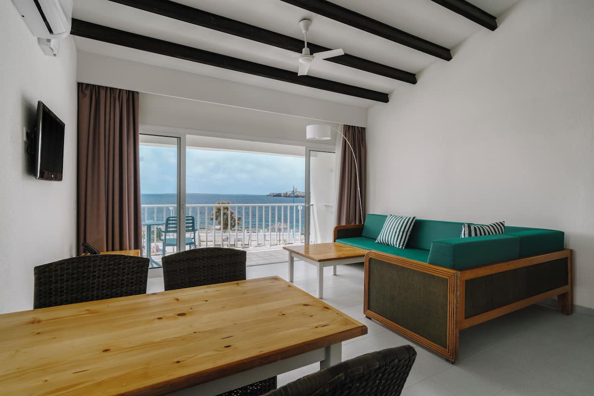 Una habitación moderna con una mesa de madera, un sofá verde con almohadones a rayas y vistas al mar a través de amplias ventanas.