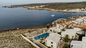 An aerial view of a coastal area with a swimming pool, white buildings, and a lighthouse in the distance. - Aluasun Far Menorca (Sant Lluis)