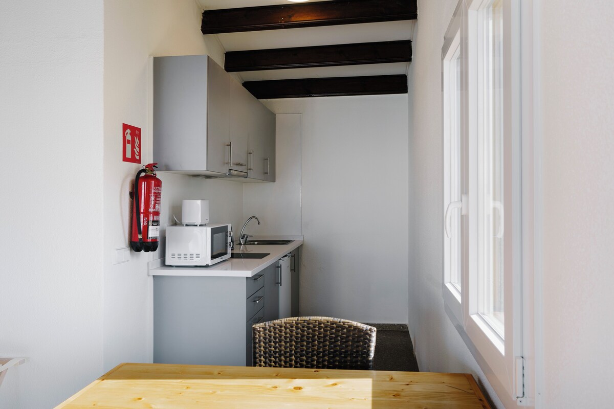 A compact kitchen with a microwave, sink, and a fire extinguisher on the wall.