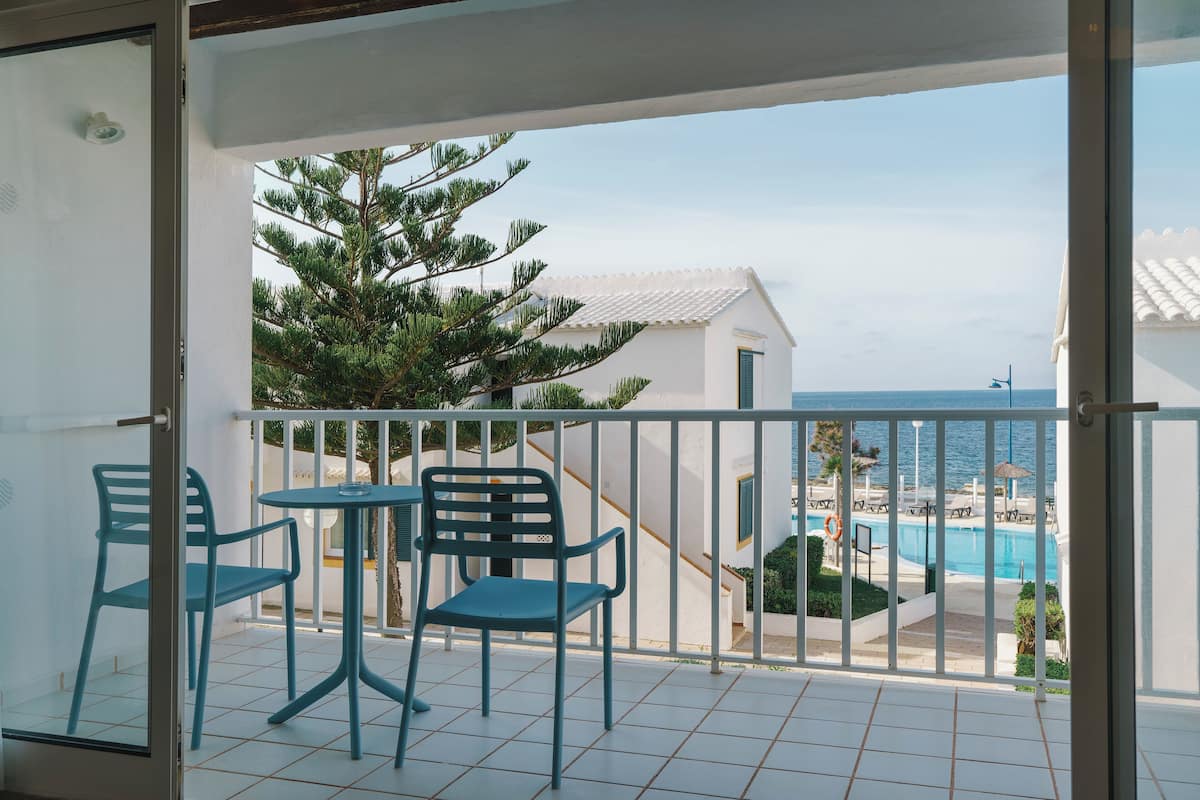 Un balcón con dos sillas y una mesa, con vistas a una piscina y una playa.