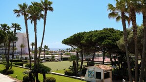 A courtyard with palm trees, a small kiosk, and a tennis court. - Aluasun Far Menorca (Sant Lluis)